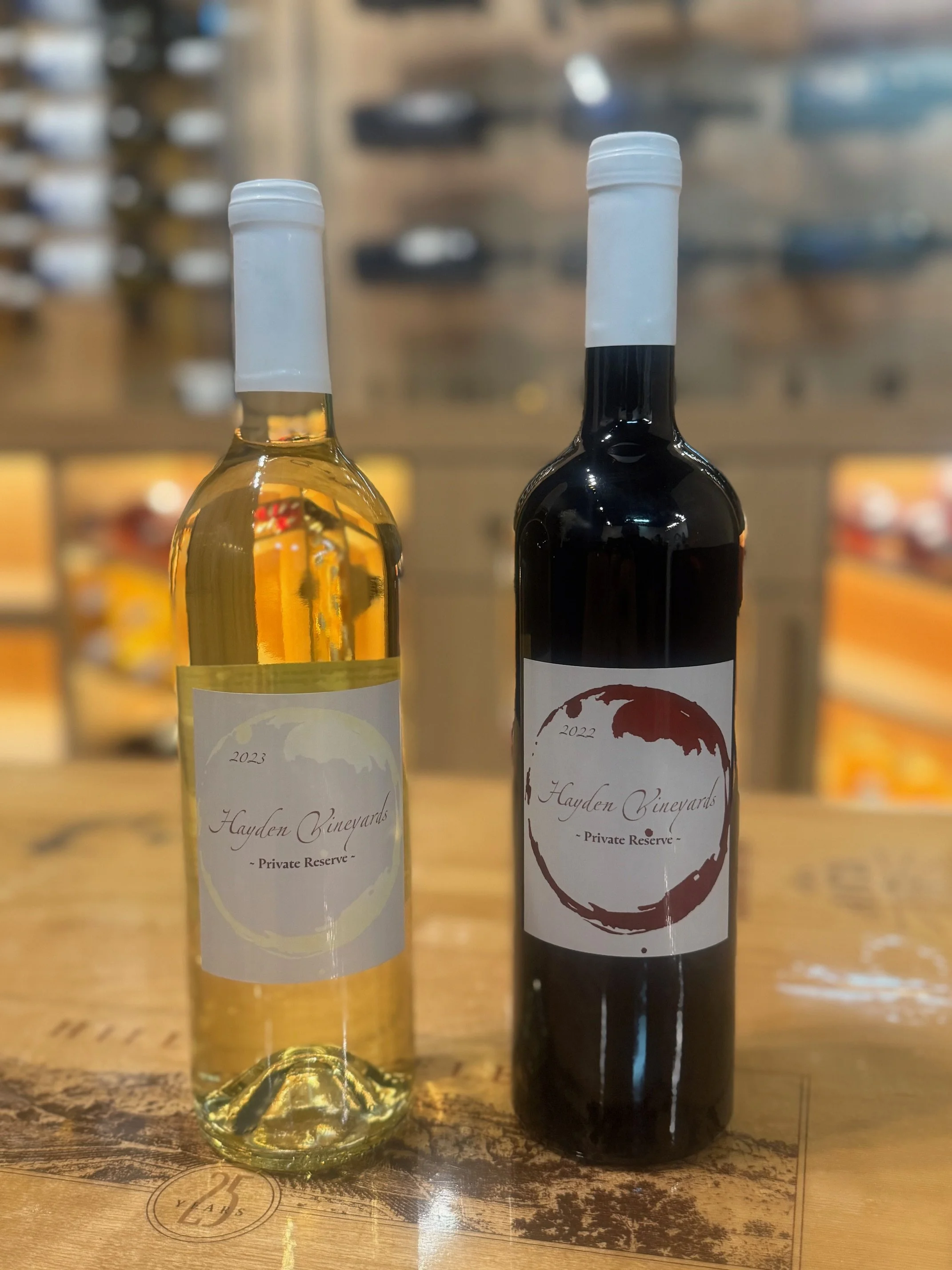 Two bottles of wine on a wooden surface, one white and one red, with labels from Hayden Vineyards.