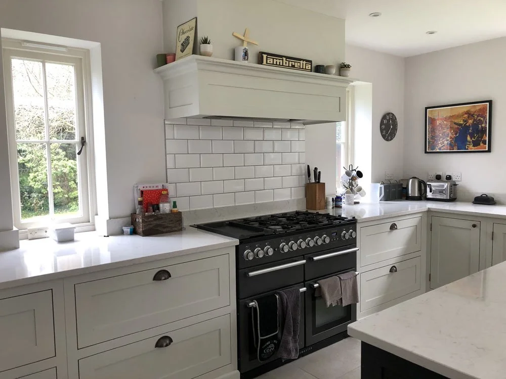 Bright kitchen with white cabinets, a stainless steel stove, and a window casting natural light. Decor includes potted plants, framed artwork, and small kitchen appliances on the counters.