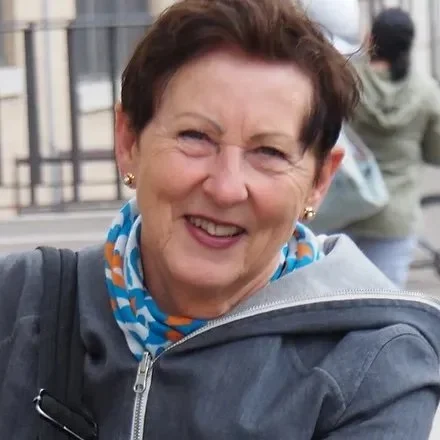 Lächelnde ältere Frau mit kurzen braunen Haaren, blaue und orange Halstücher, graue Jacke, im Freien