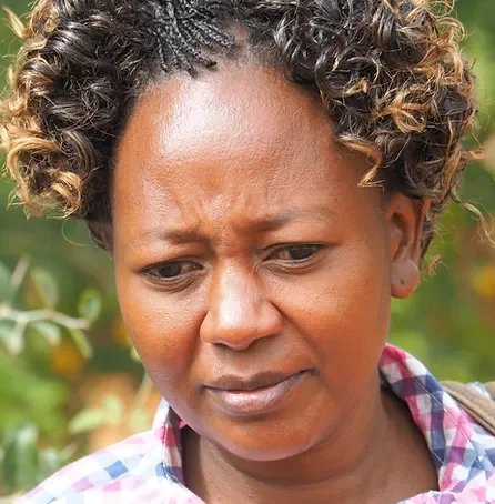 Eine Frau mit lockigem Haar schaut nachdenklich auf ein Feld mit grünen Pflanzen.