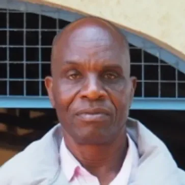 Porträt eines Mannes vor einem schwarzen Gitter und Fahrzeug, trug ein weißes Hemd und eine helle Jacke.