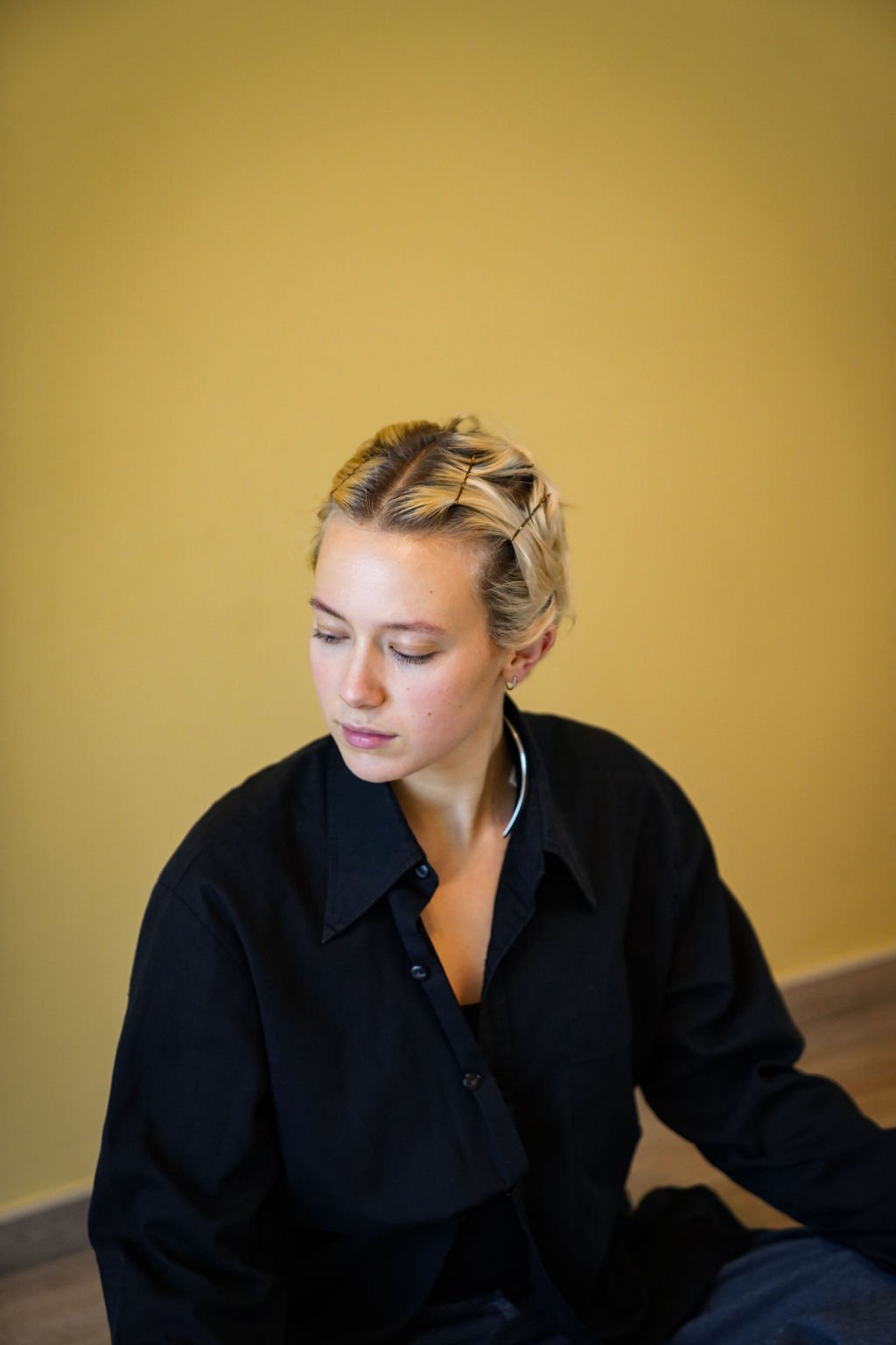 Vrouw met kort haar, zittend in een lichte kamer, is yoga aan het doen.