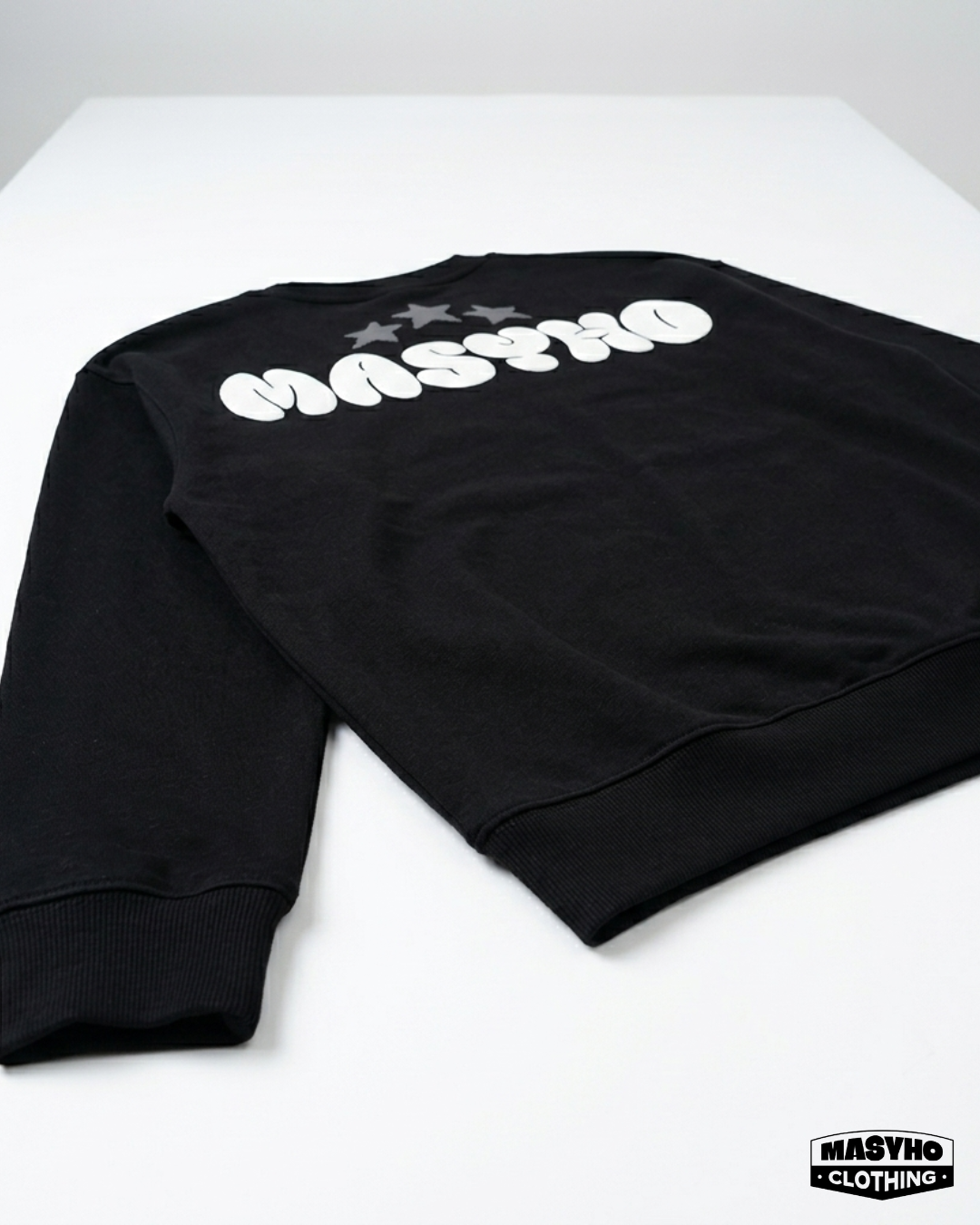 Black sweatshirt with white text 'MASHO' and stars on a white surface, with a 'MASHO CLOTHING' logo in the bottom right corner.