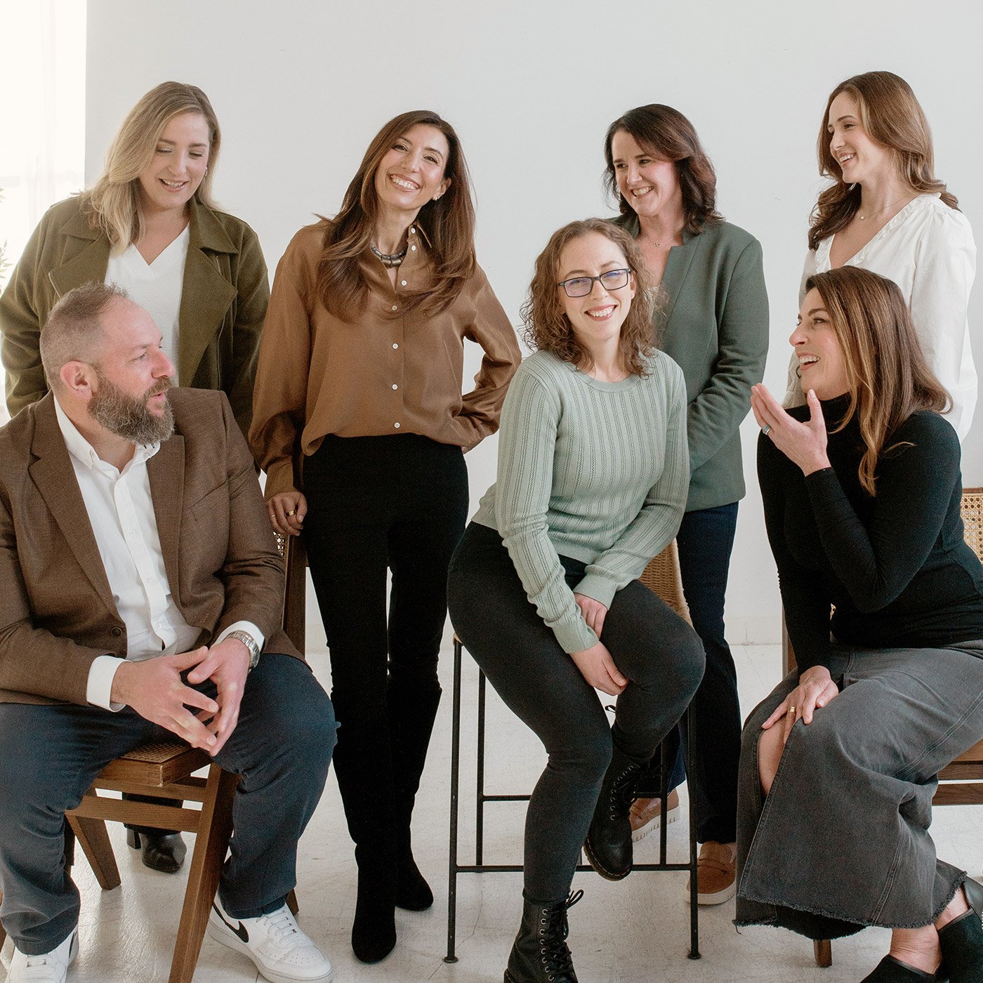 The Garnish team. Group of seven diverse women and one man in a casual office setting, smiling and engaged in conversation.