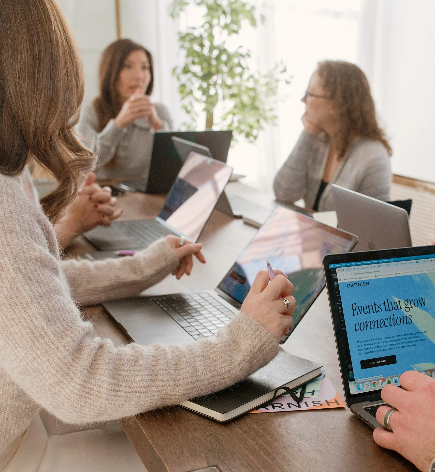 The Garnish team sitting around a wooden table in a meeting room, working on laptops and discussing ideas, with a large window and plants in the background.
