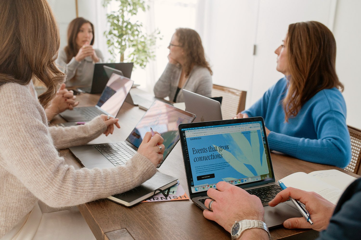 The Garnish team. A group of women sitting around a conference table using laptops and taking notes during a meeting.