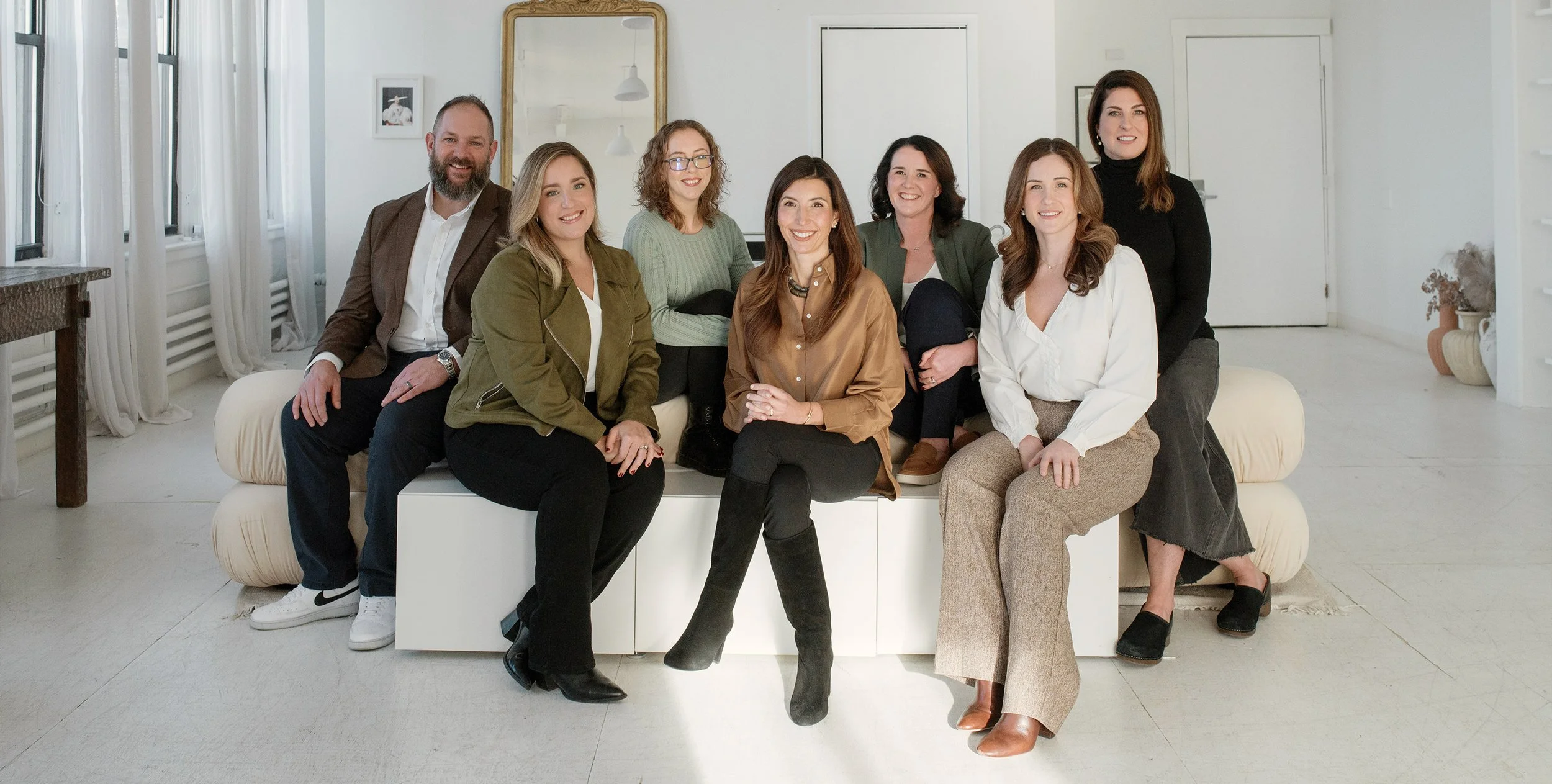 Picture of the Garnish team. Group of eight diverse young adults sitting and standing in a bright, modern living room, smiling at the camera.
