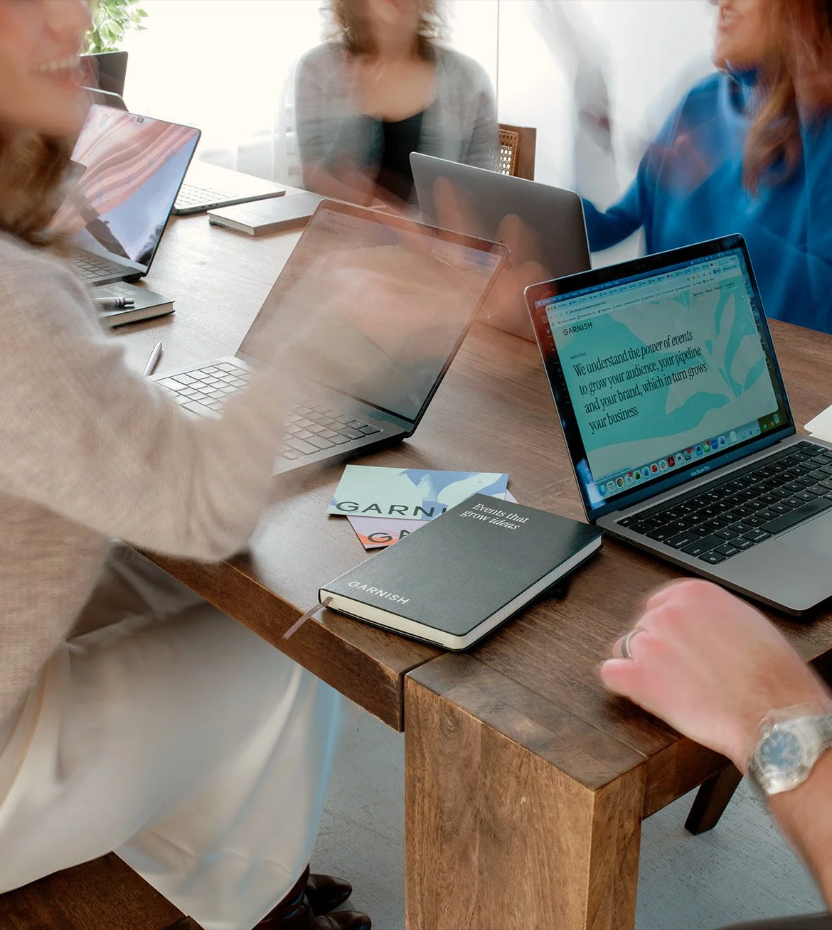 The Garnish team seated around a wooden table working on laptops with notebooks and Garnish promotional cards on the table, engaged in a discussion or meeting.