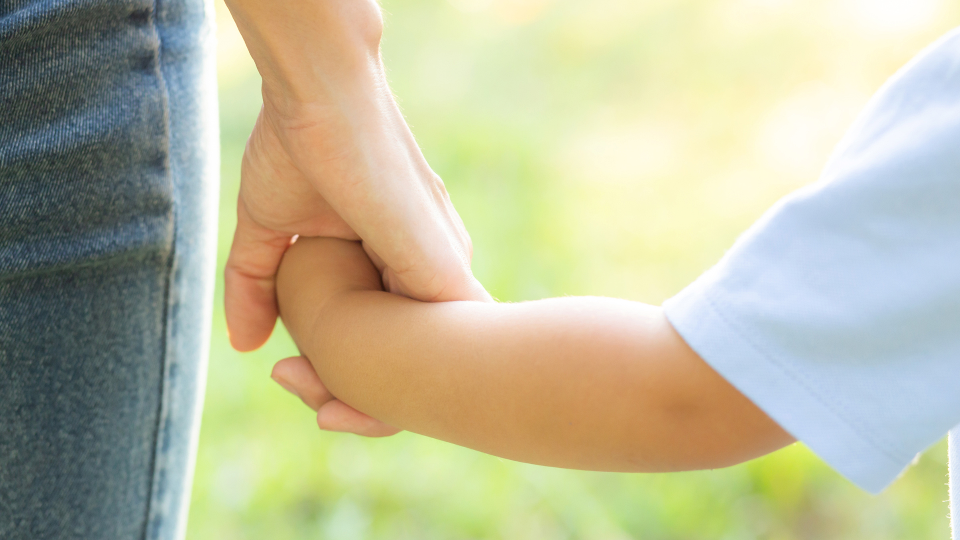 Close-up of an adult holding a child's hand outside in natural light