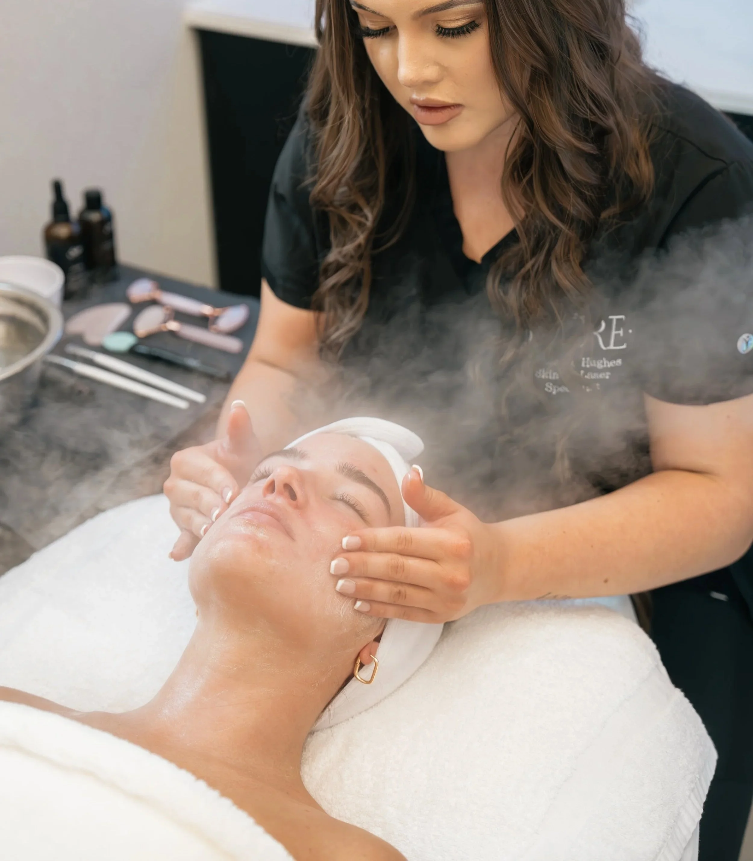 A woman receiving a facial treatment at a spa or skincare clinic, with steam or vapor rising during the procedure.