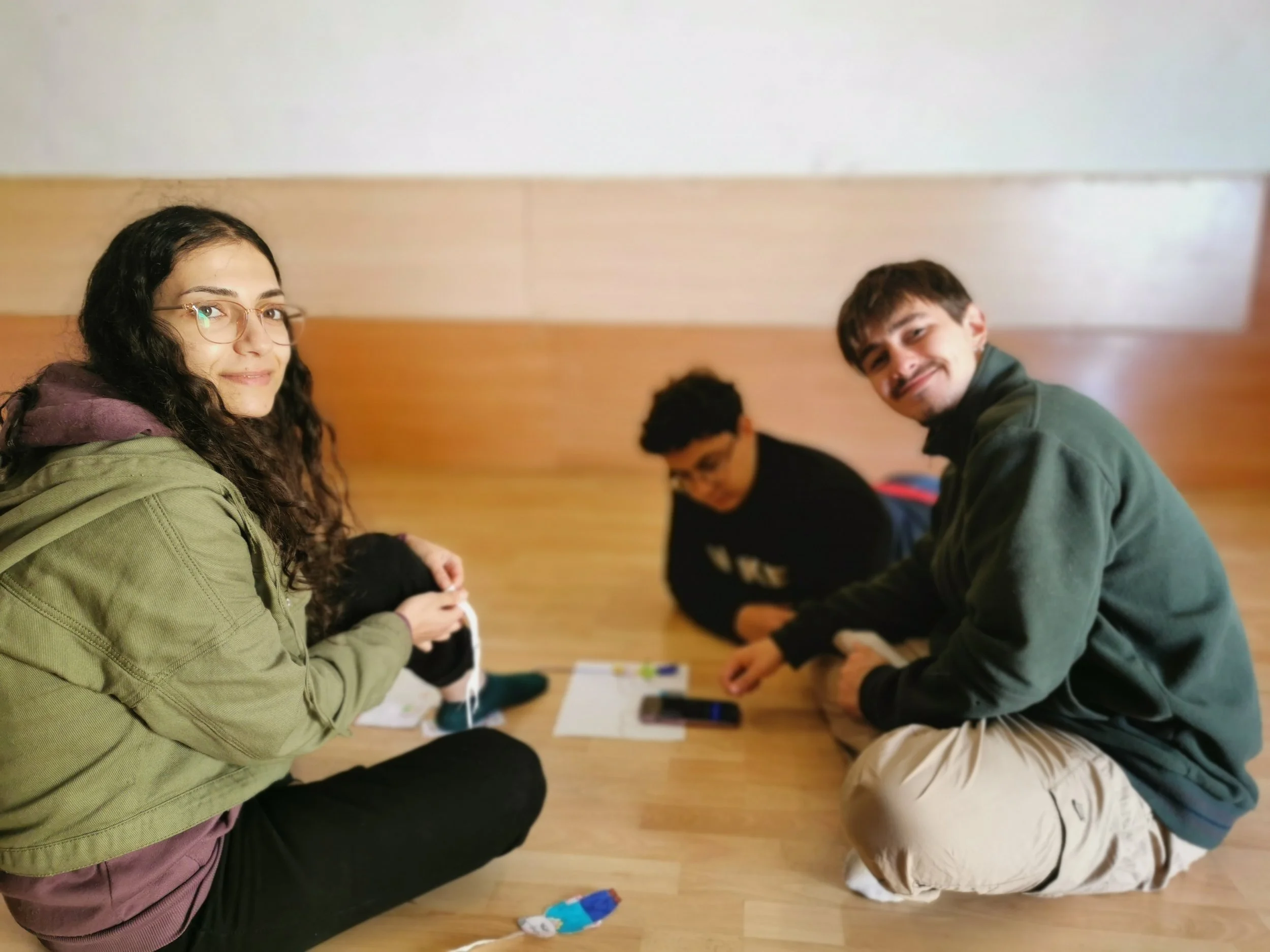 Tres jóvenes trabajando en círculo miran a cámara y sonríen. 