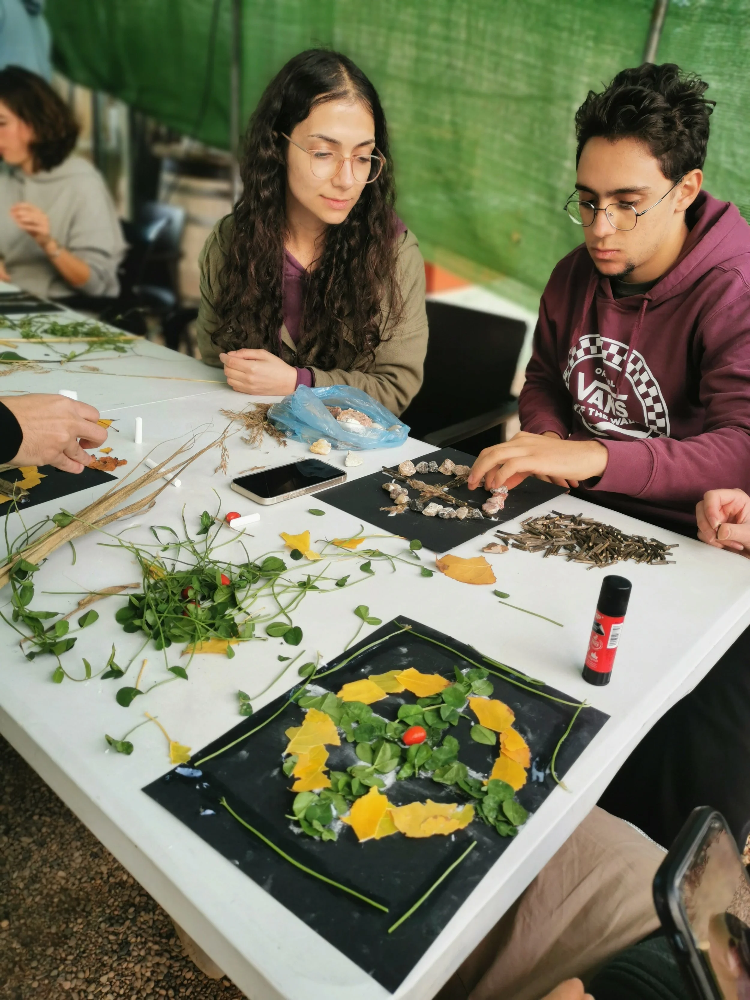 Jóvenes crean con elementos naturales en círculo en una mesa. 
