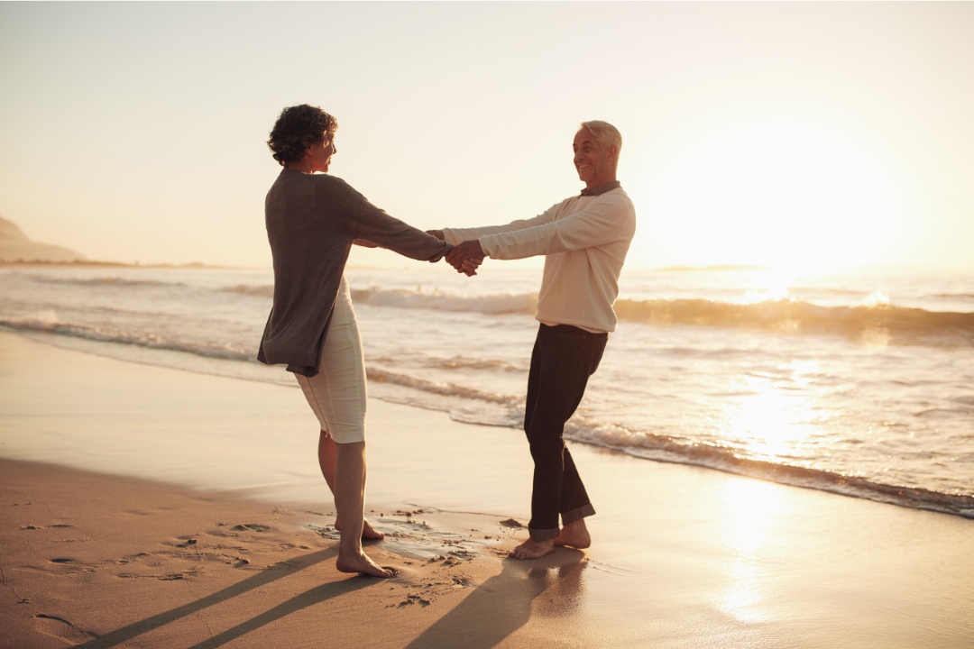A couple holding hands on the beach during sunset.
