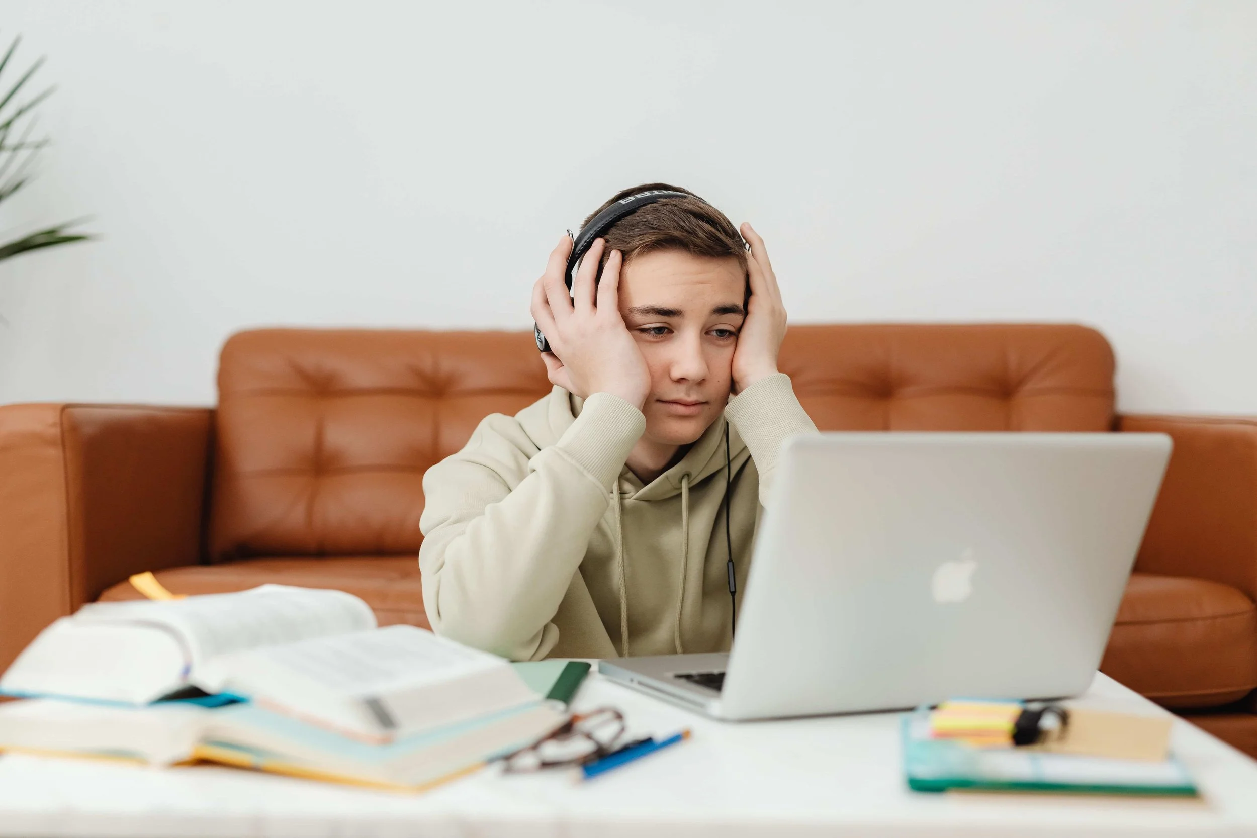 Young person struggling to concentrate at a laptop with books around them, representing brain fog and cognitive effects of poor sleep and glymphatic dysfunction