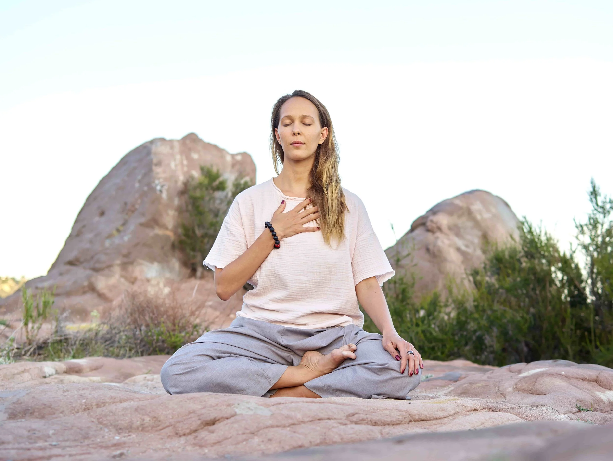 Woman meditating outdoors with her hand resting on her chest, practicing body awareness and grounding