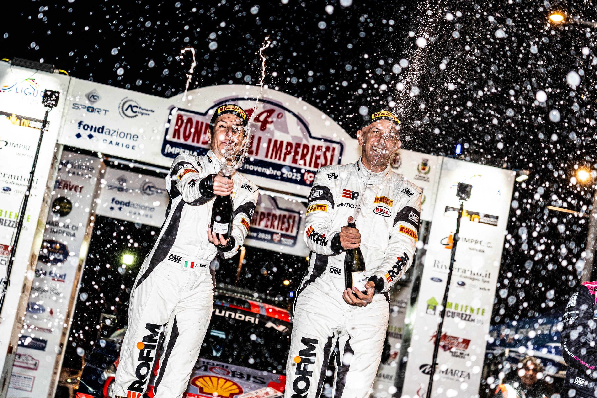 Due piloti di rally sul podio celebrano la vittoria con champagner sotto una pioggia di bolle, in occasione di un rally.