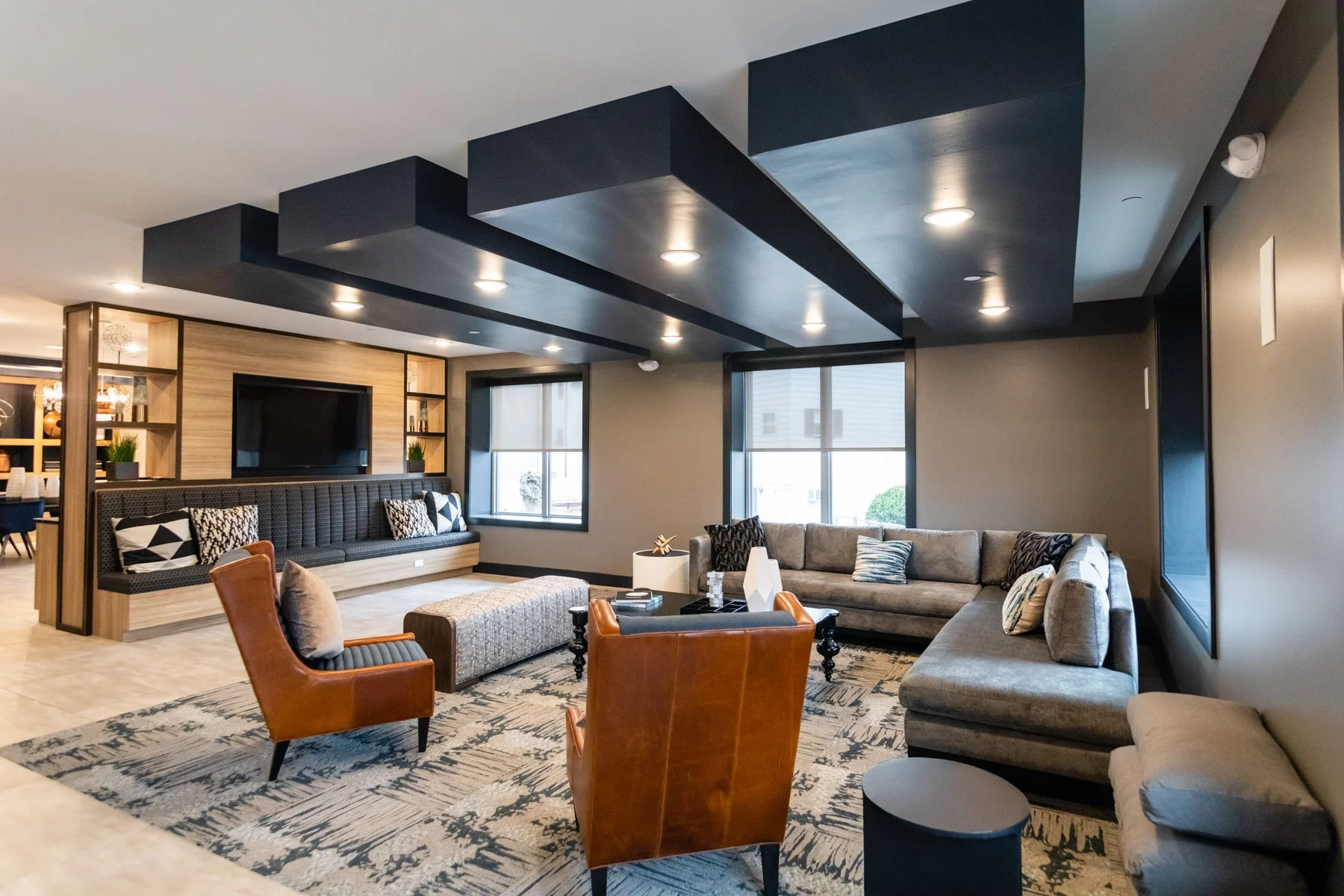 Modern living room with gray sectional sofa, leather armchair, patterned rug, and ceiling with black geometric accents