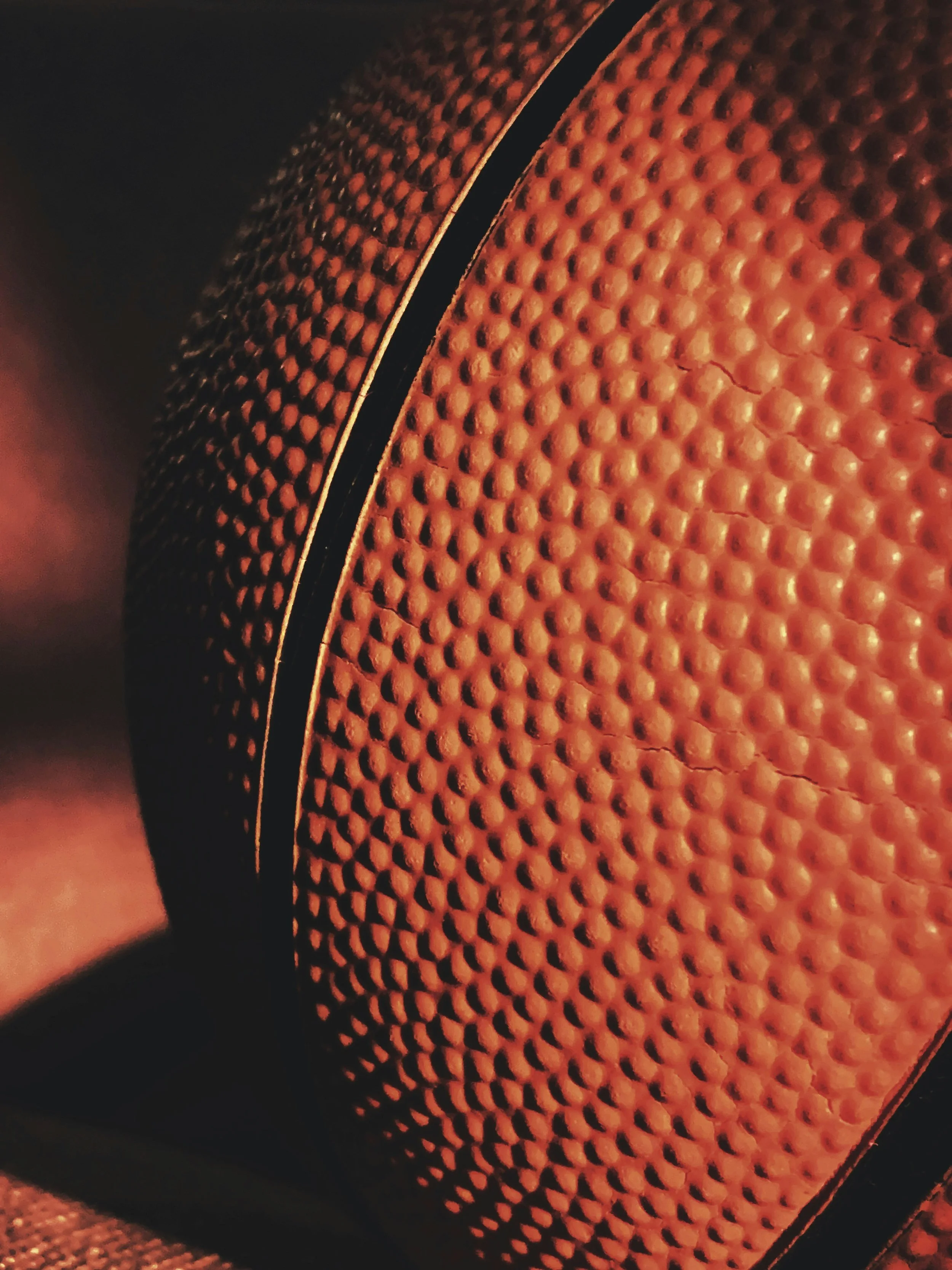A close-up of a textured basketball with orange surface and black lines.