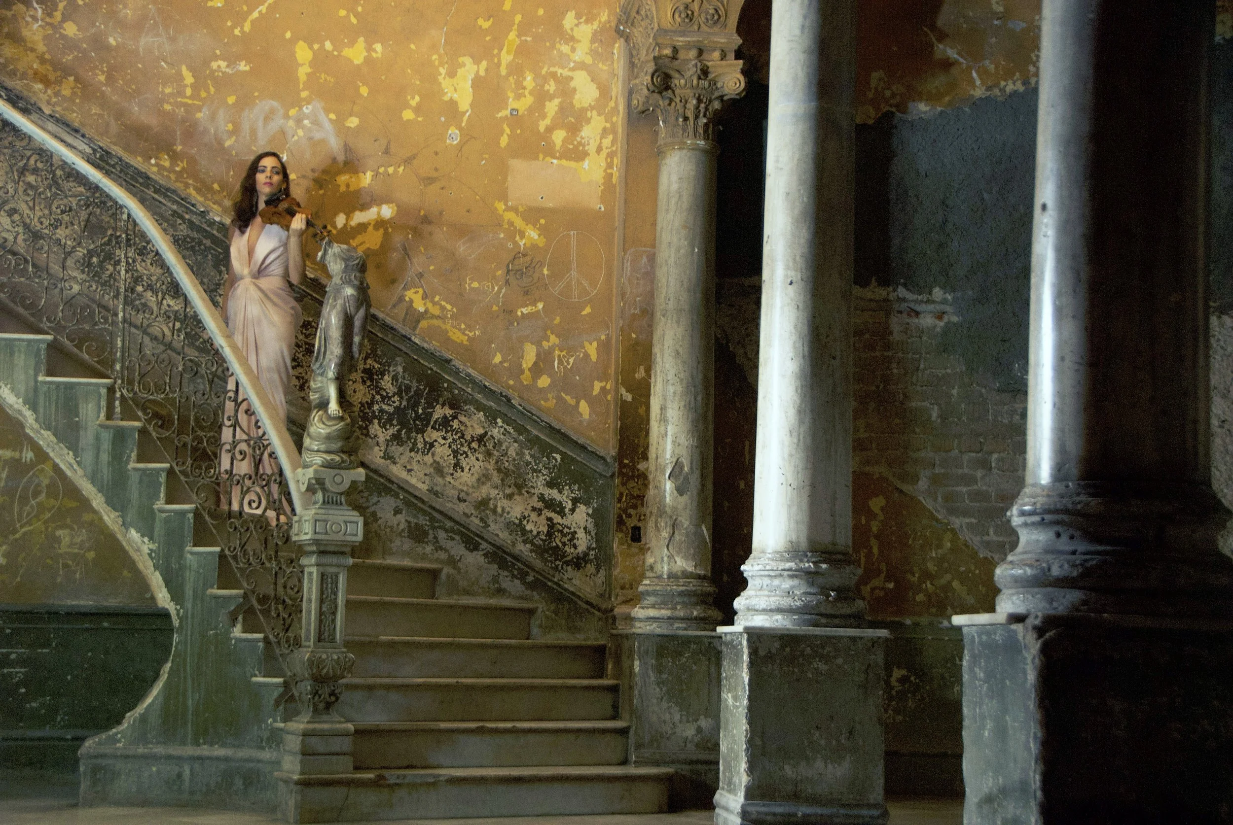 Rebecca Cherry, Founder of Rebecca Cherry Music in an old building wearing a light pink gown and holding her violin in Cuba.