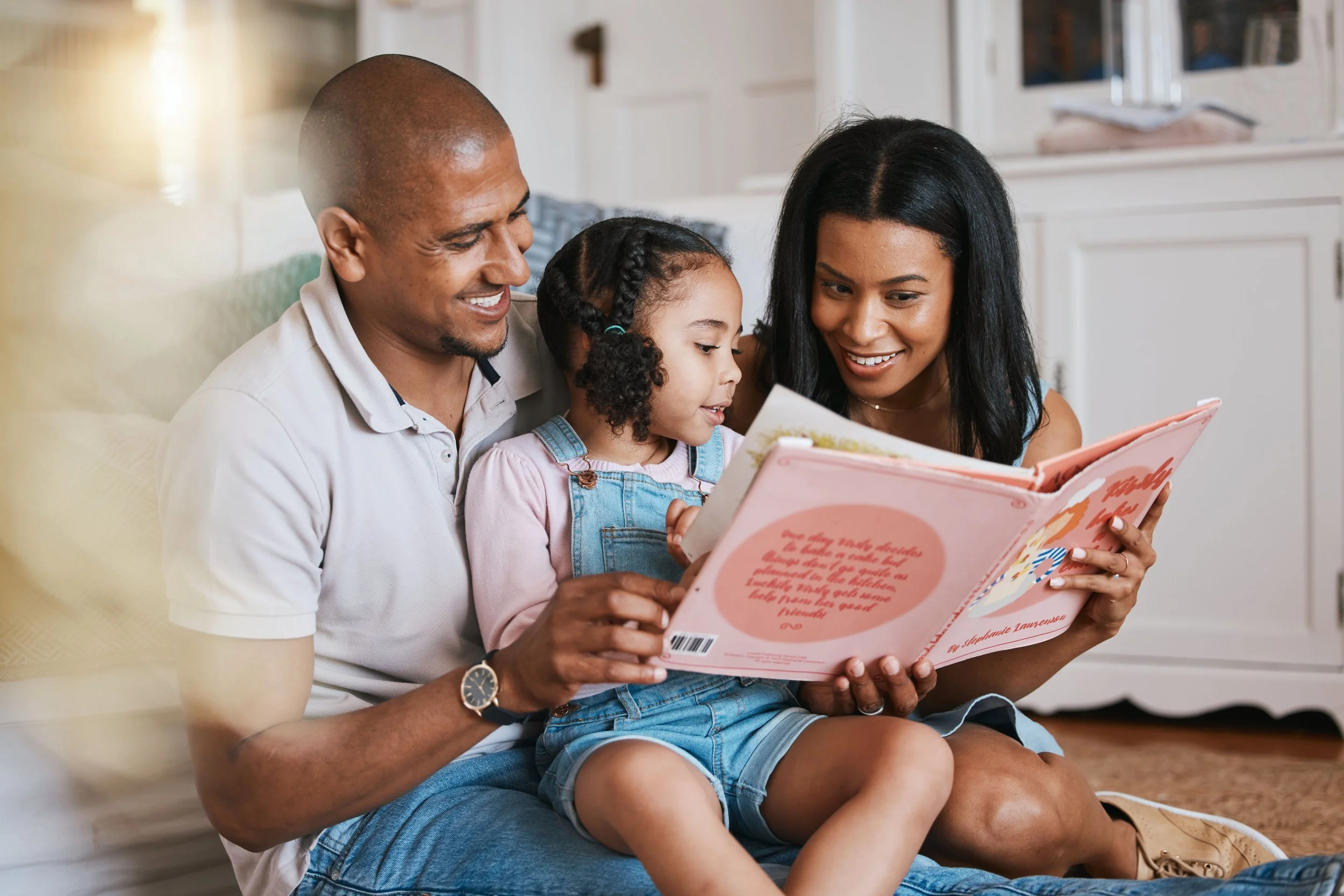 A family of three sitting on the floor, reading a storybook together in a cozy home setting.