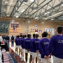 A line of students wearing purple uniforms standing in a gymnasium during a school event.