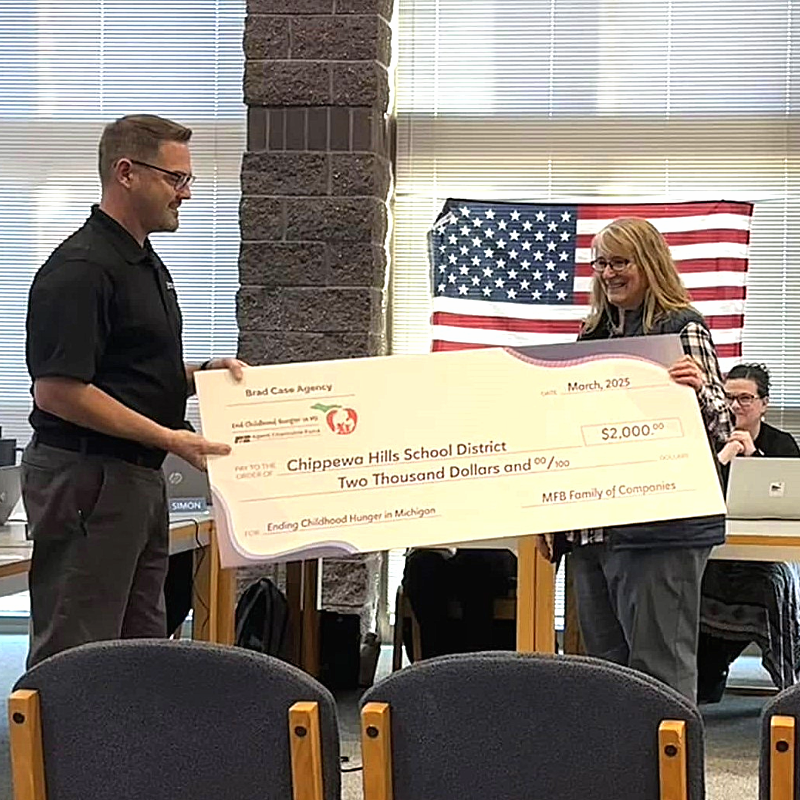 A man presenting a large check to a woman in a room with an American flag in the background.