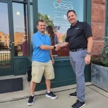 Two men shaking hands outside a building on a city sidewalk.