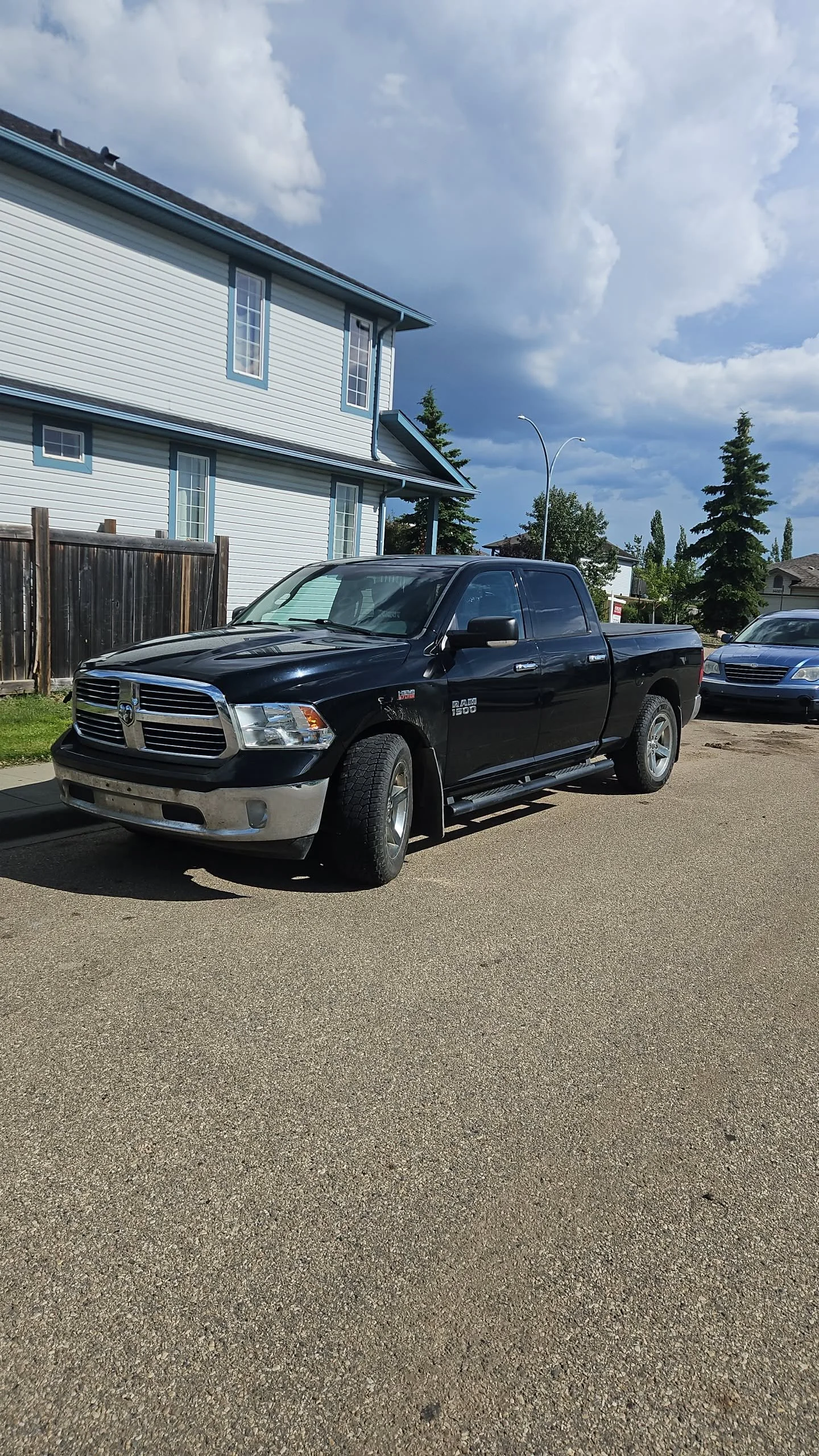 Black RAM 1500 pickup truck parked on a residential street with houses and trees in the background.