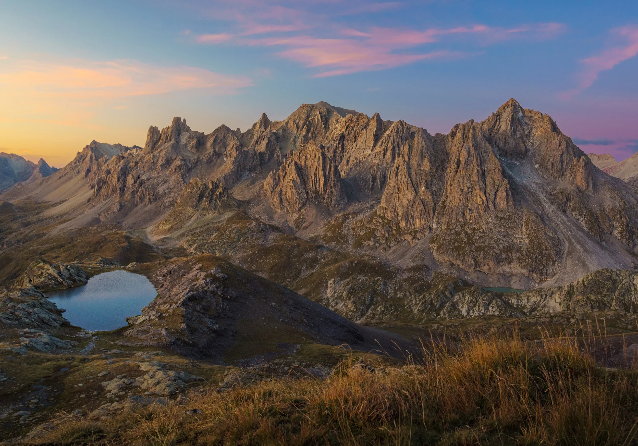 Montagnes rocheuses du Queyars, les crêtes de la Taillante, sous un ciel coloré avec un petits lac, le lac Foréant, en premier plan.