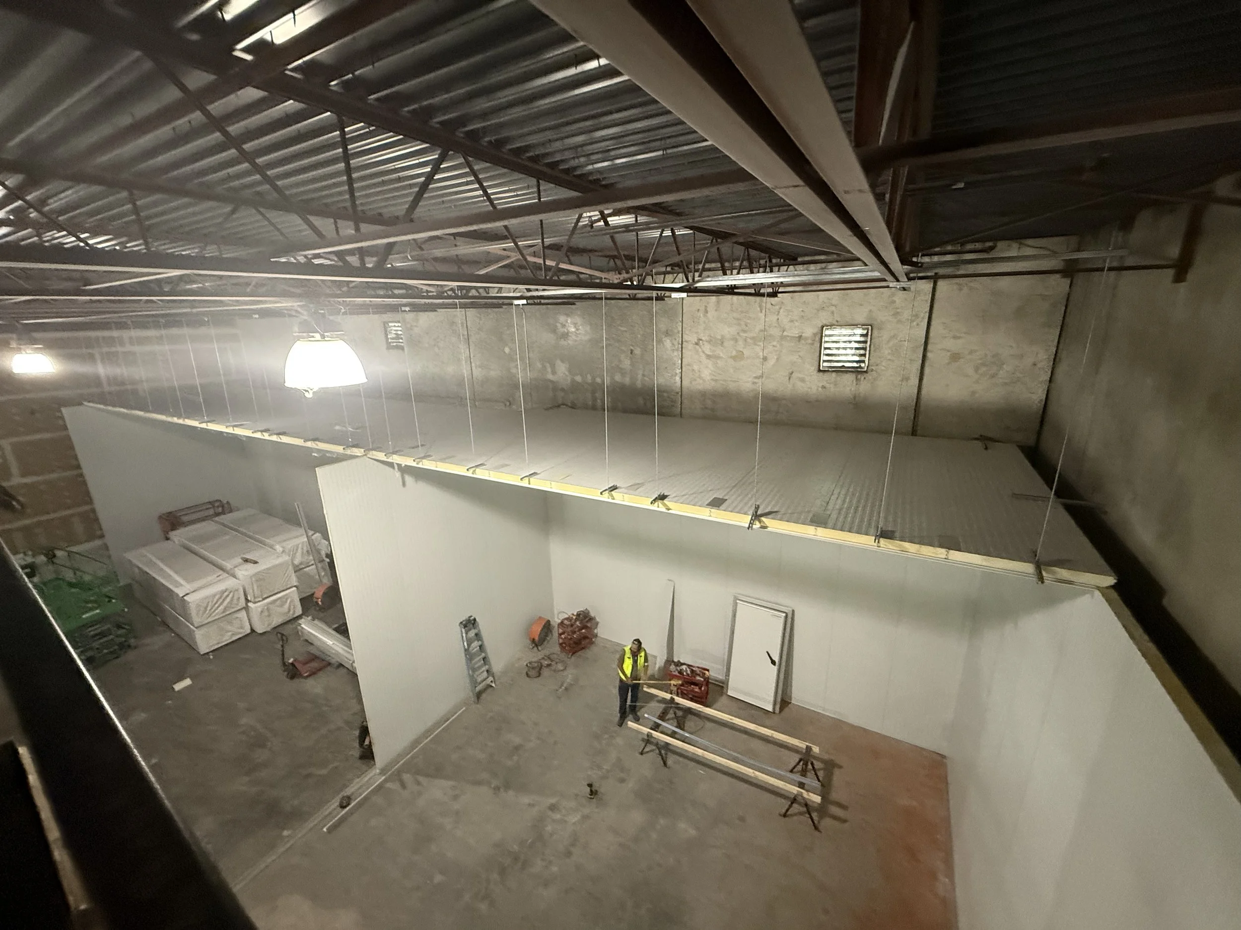 Interior view of a construction site with partially built walls and a worker in a high-visibility vest.