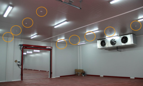 Empty industrial space with white walls, red trim, and ceiling lights, with a roll-up door and ventilation fans on the wall.