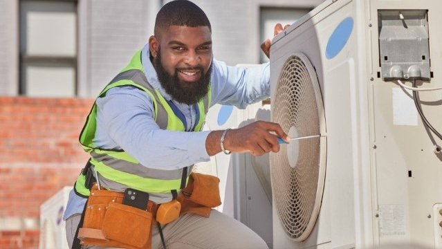 Technician repairing an air conditioning unit on a building's exterior.