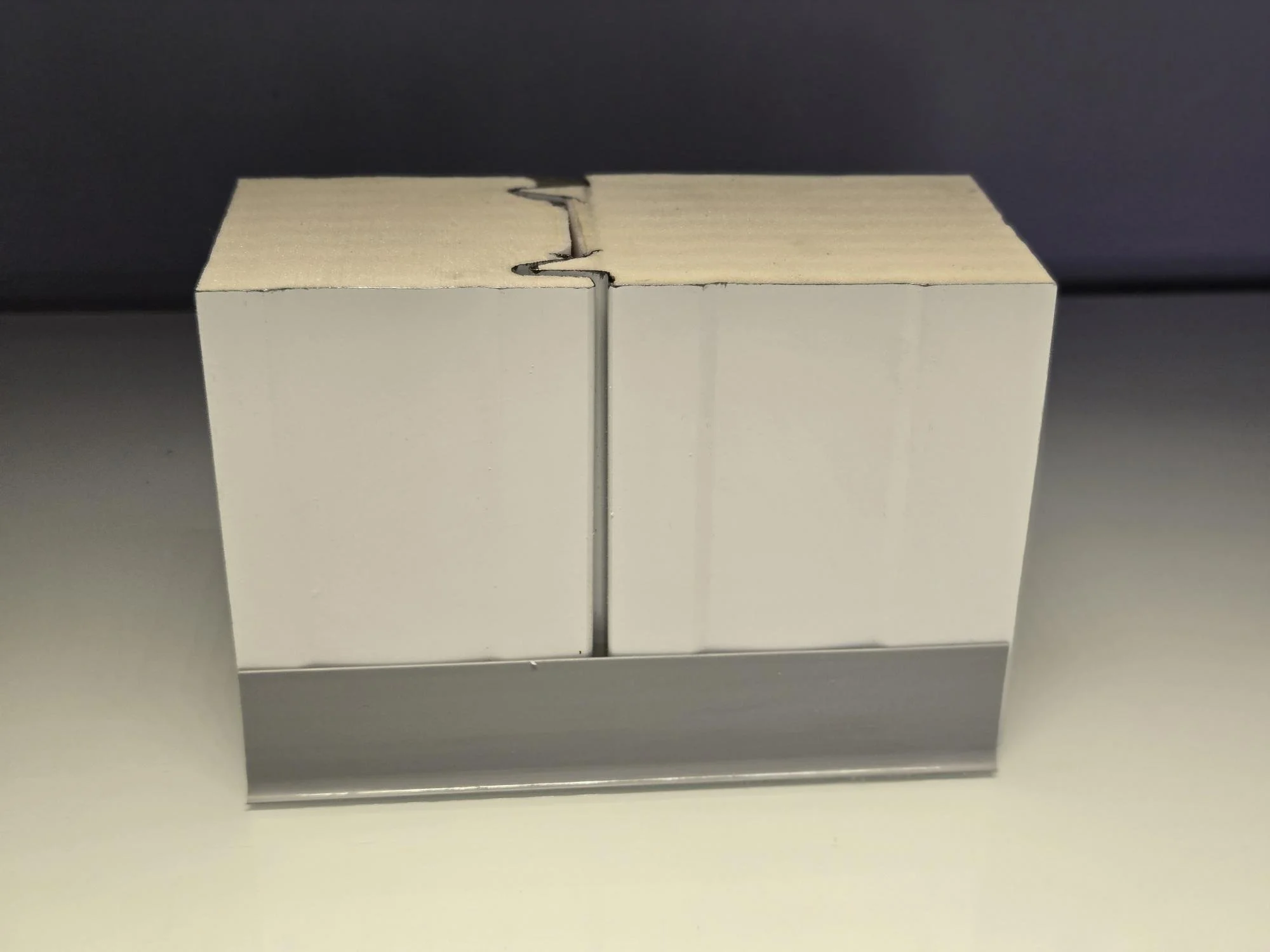 Close-up of a white cardboard box with a metal strip at the bottom, sealed with black tape, against a dark background.