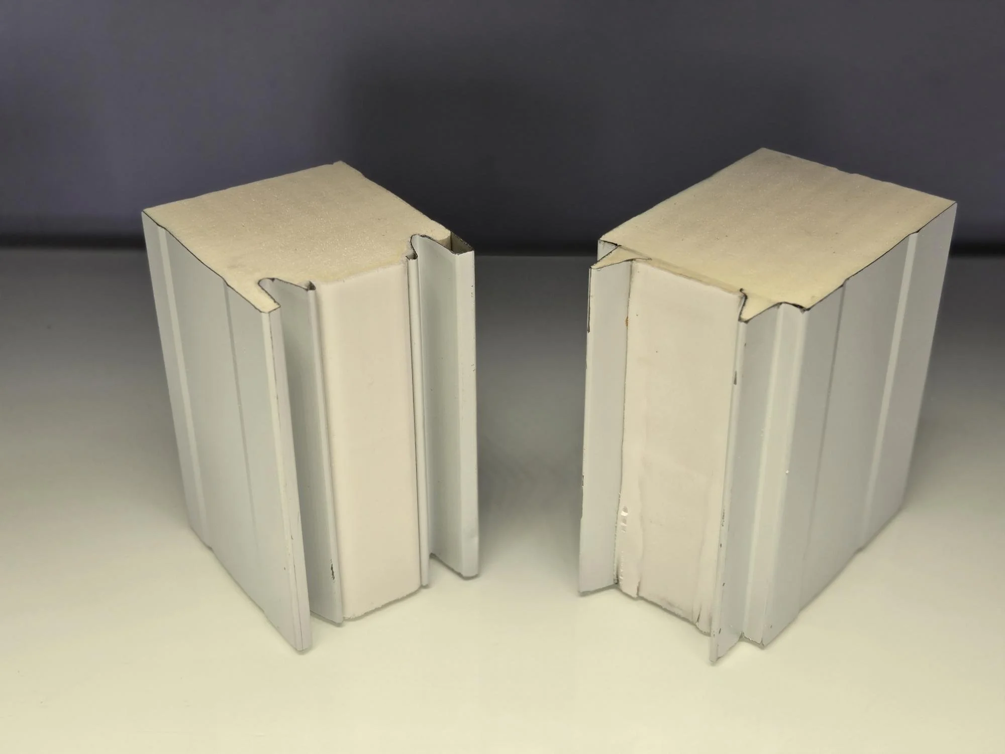 Two aluminum extrusion pieces with T-slots and internal foam padding on top, placed on a flat surface against a gray background.