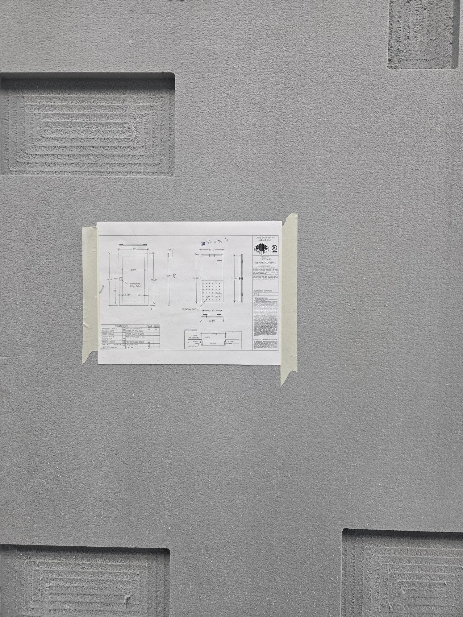 Blueprint or technical drawing taped to a gray wall with textured patterns and vents.