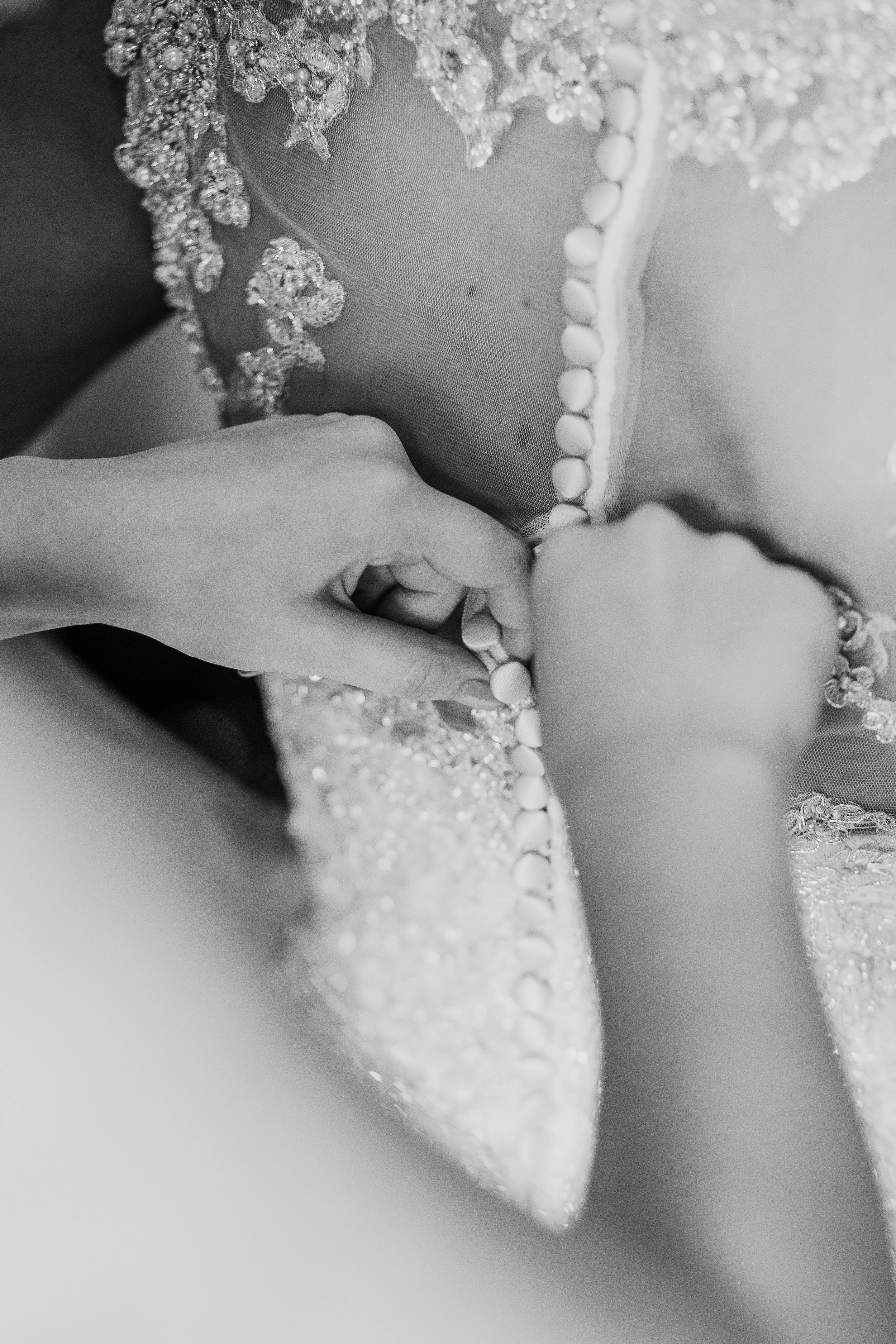 Black-and-white close-up of a bride and groom exchanging wedding rings, with lace and beaded clothing visible.