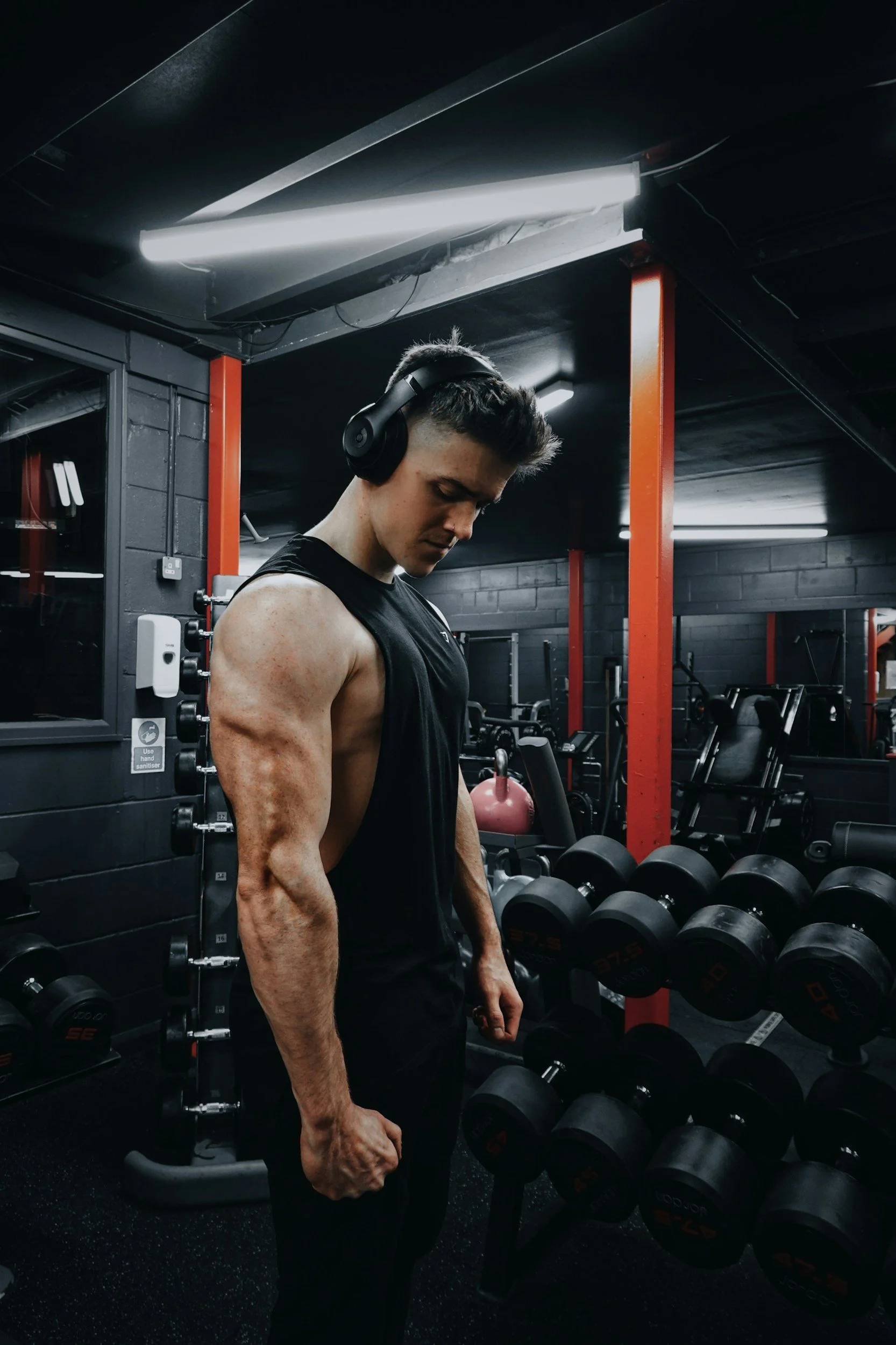 A young man with muscular arms wearing headphones in a gym.