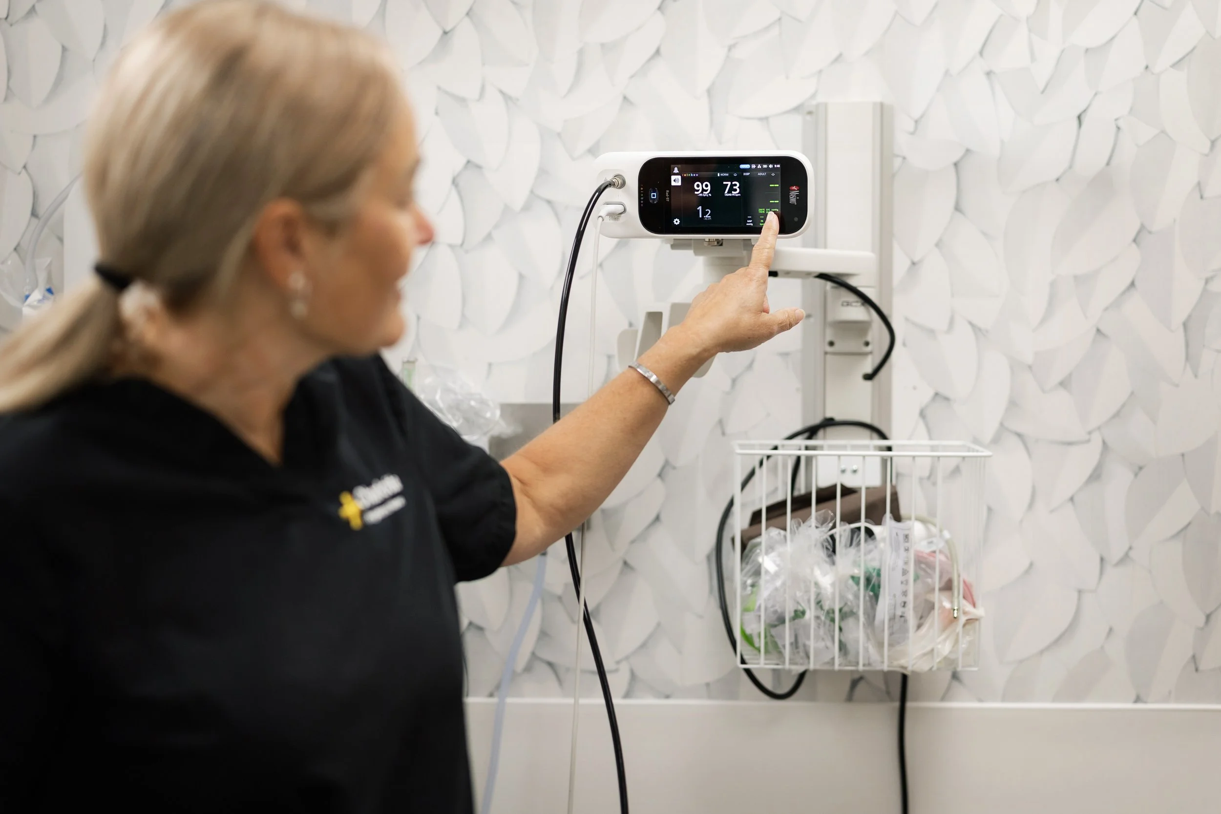A healthcare professional adjusting a patient monitor with vital signs in a medical setting.
