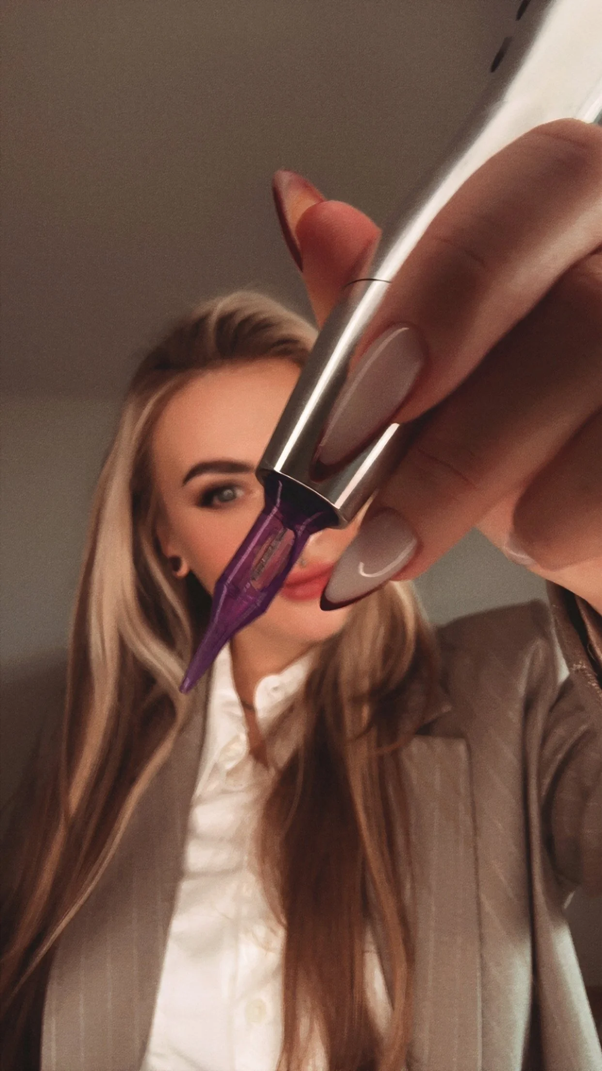 Eine Frau hält eine Hand-Haarzange mit einer schwarzen Unterseite und einer lila Spitze vor das Gesicht, während sie ein Selfie macht.