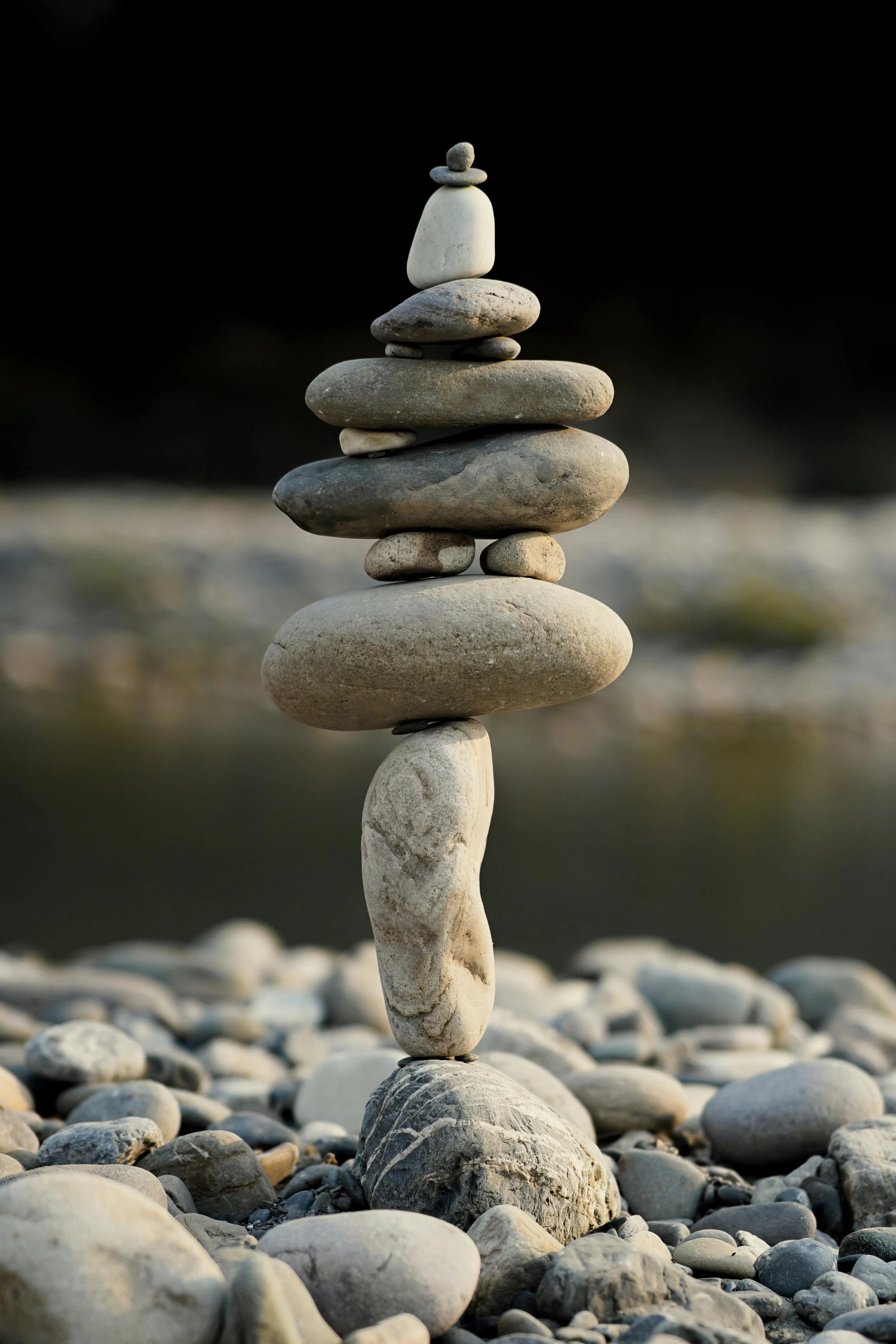 A balanced stack of various-sized smooth stones on a pebbled surface, with a dark blurred background.