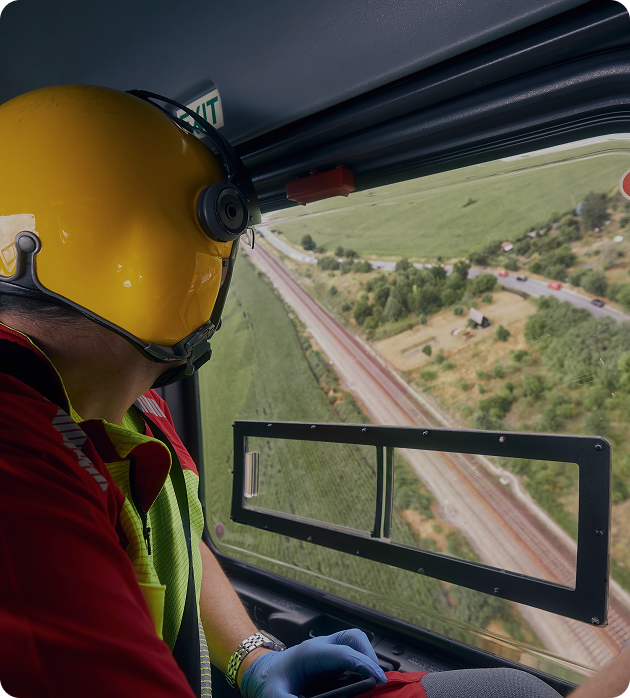 Emergency response pilot in a yellow helmet observing the terrain from a helicopter