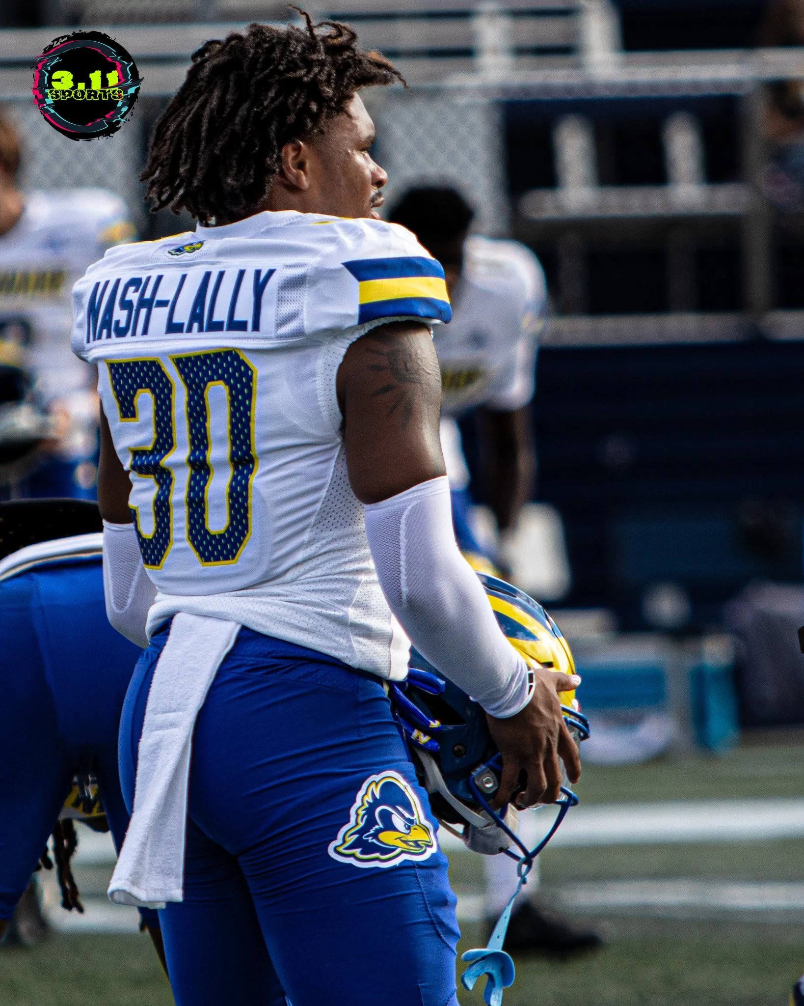 American football player wearing jersey number 30 with the name Nash-Lally, holding a helmet, standing on a football field during a game or practice.