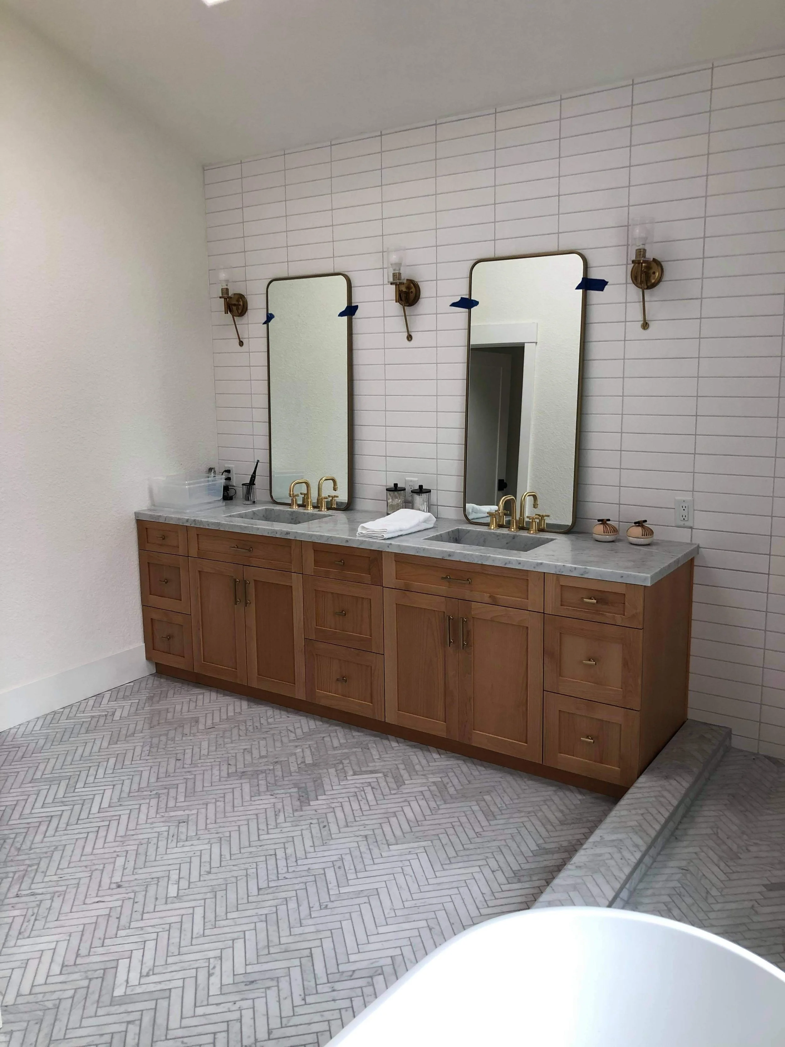 Modern double vanity installation with marble countertop, gold faucets, wood cabinetry, and wall-mounted mirrors in a remodeled bathroom – professional finish by licensed contractor in San Diego