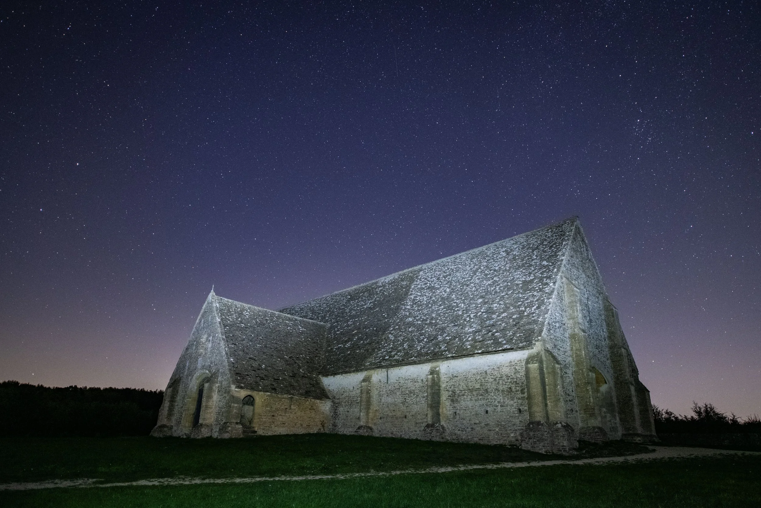 Night sky filled with stars above an old stone church with a steep roof.