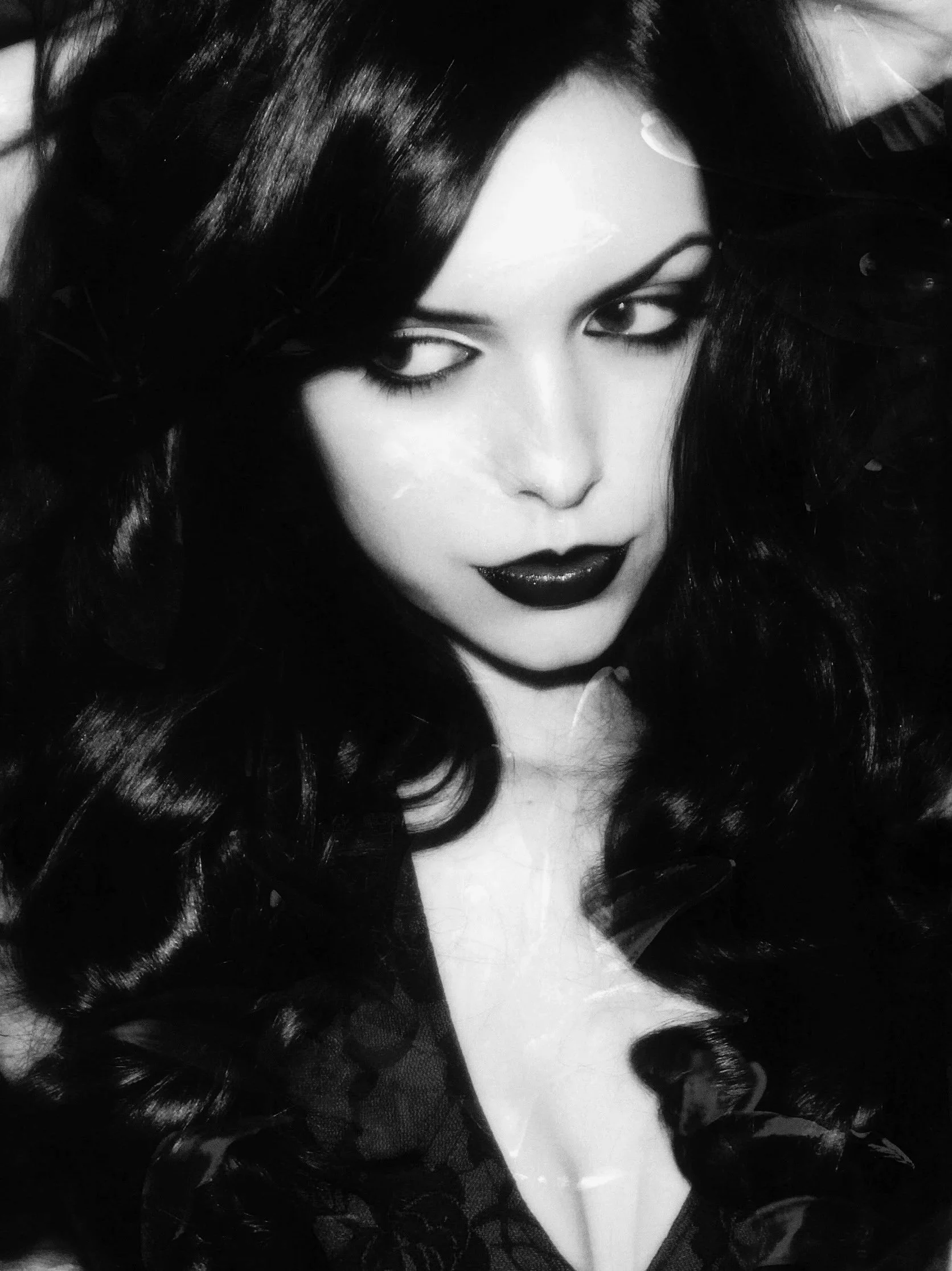 Black and white close-up photograph of a woman with long, wavy hair, dark lipstick, and intense eye makeup.