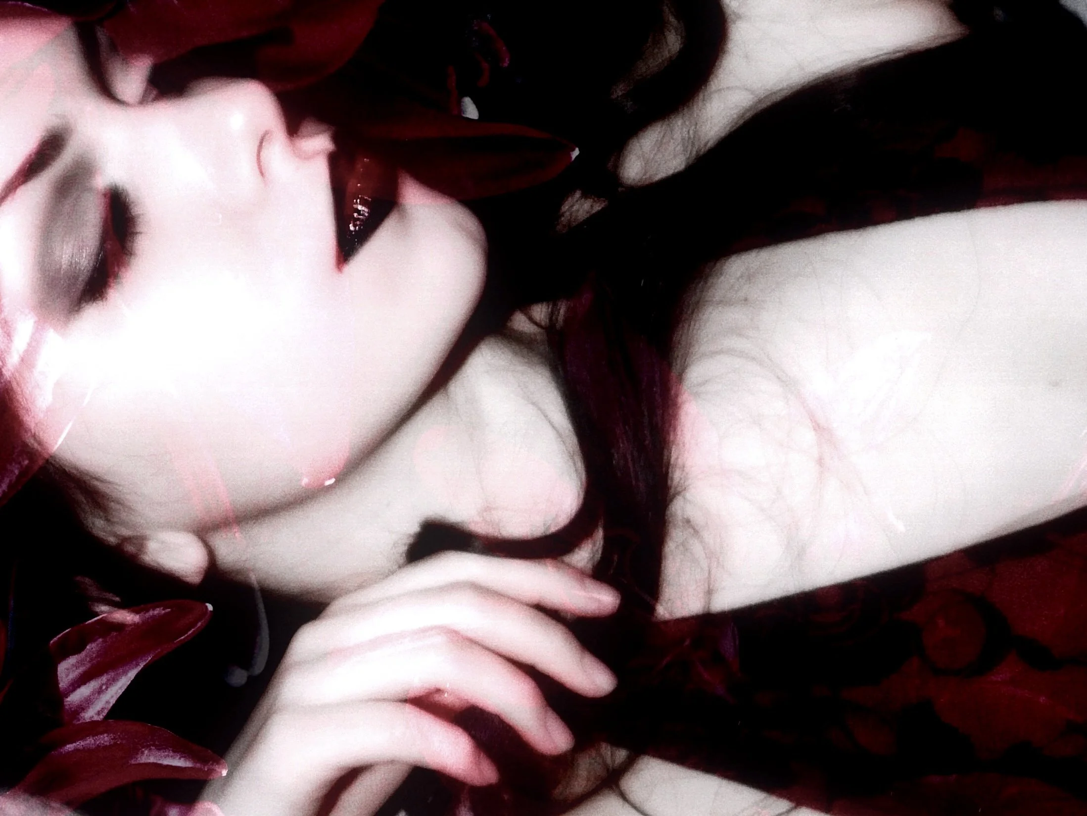 Close-up of a woman with pale skin and dark hair, wearing dark makeup, partially covered by red and black fabric.