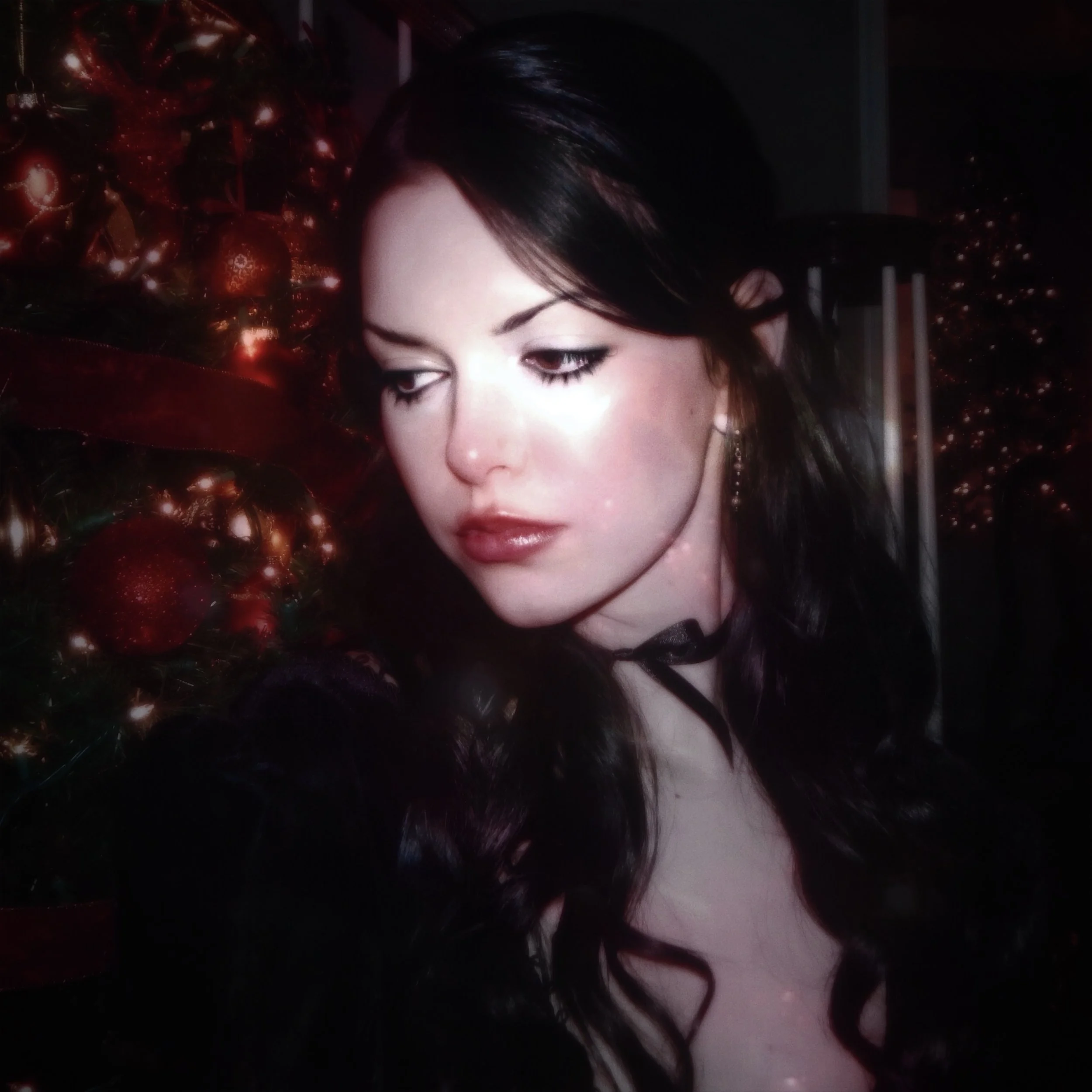 A woman with dark hair and makeup near decorated Christmas trees with red ornaments.