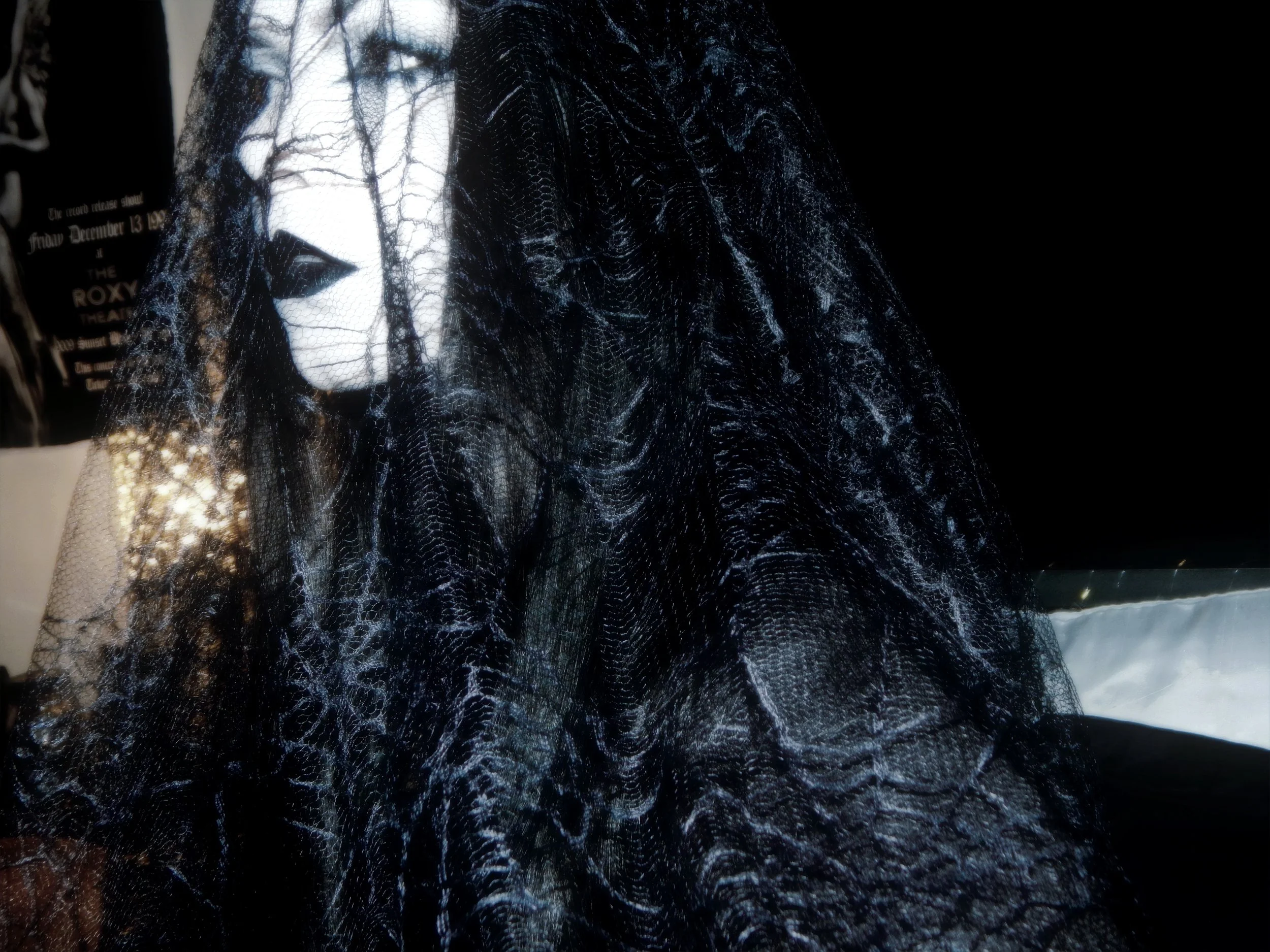 A mannequin with a painted face wearing a veil of black spiderweb-like material, with dark makeup and long black hair.