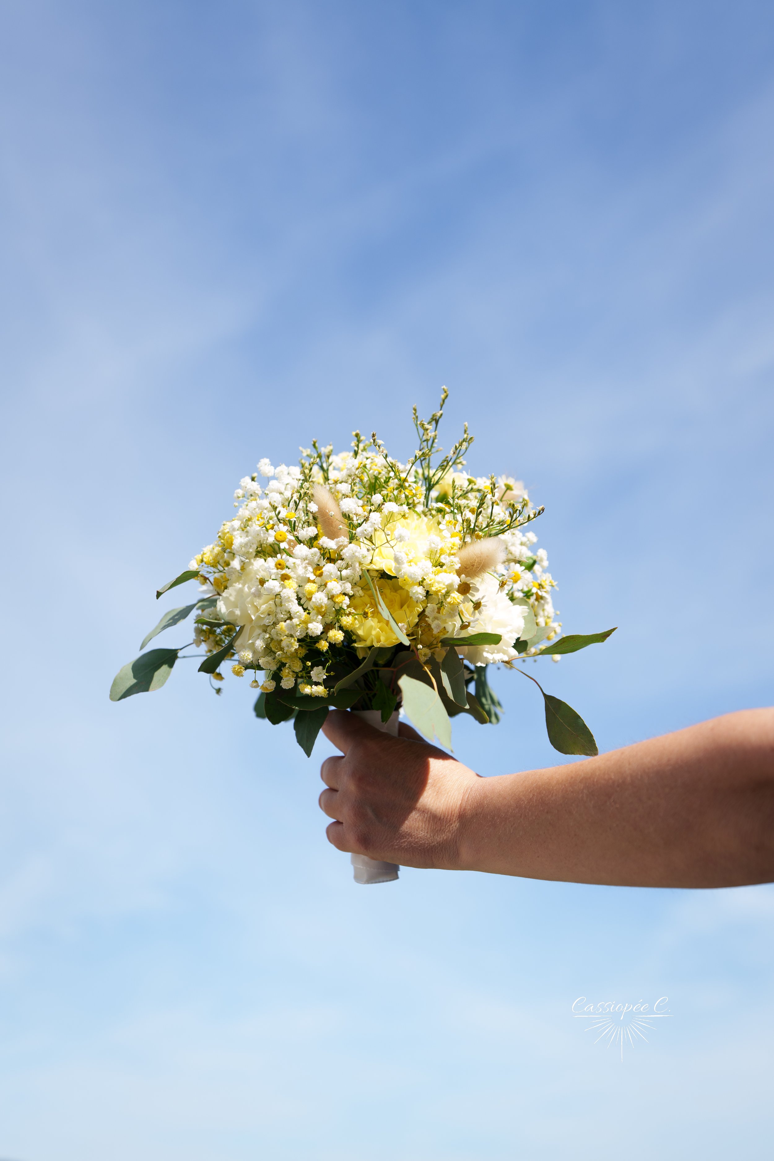 Main tenant un bouquet de fleurs blanches et jaunes avec un fond de ciel bleu