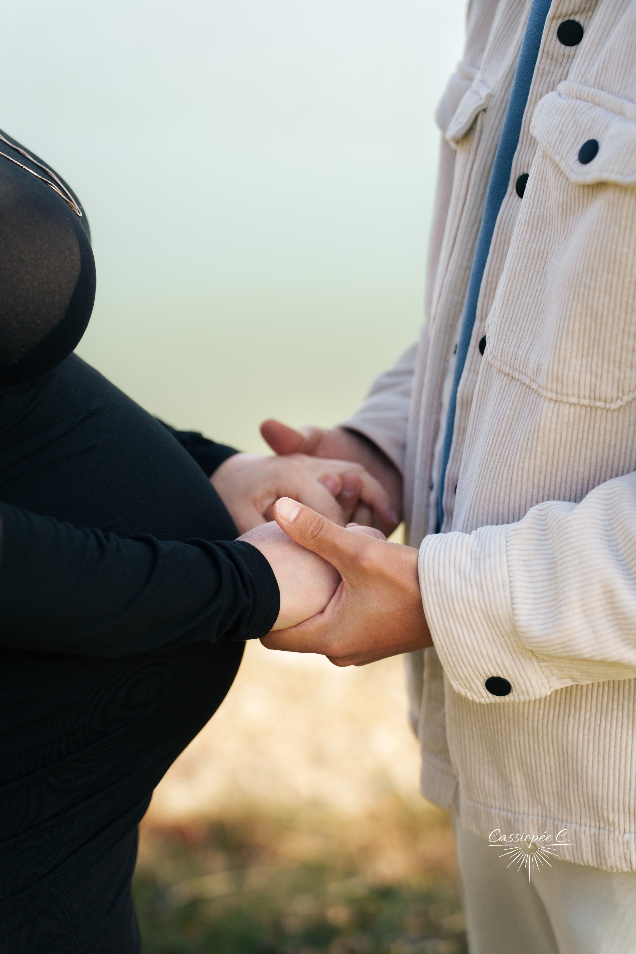 Deux personnes tenant leurs mains l'une de l'autre dans un geste de soutien. L'une porte un pull noir, l'autre un cardigan beige clair avec des boutons noirs. Le fond est flou avec des couleurs chaudes et naturelles.